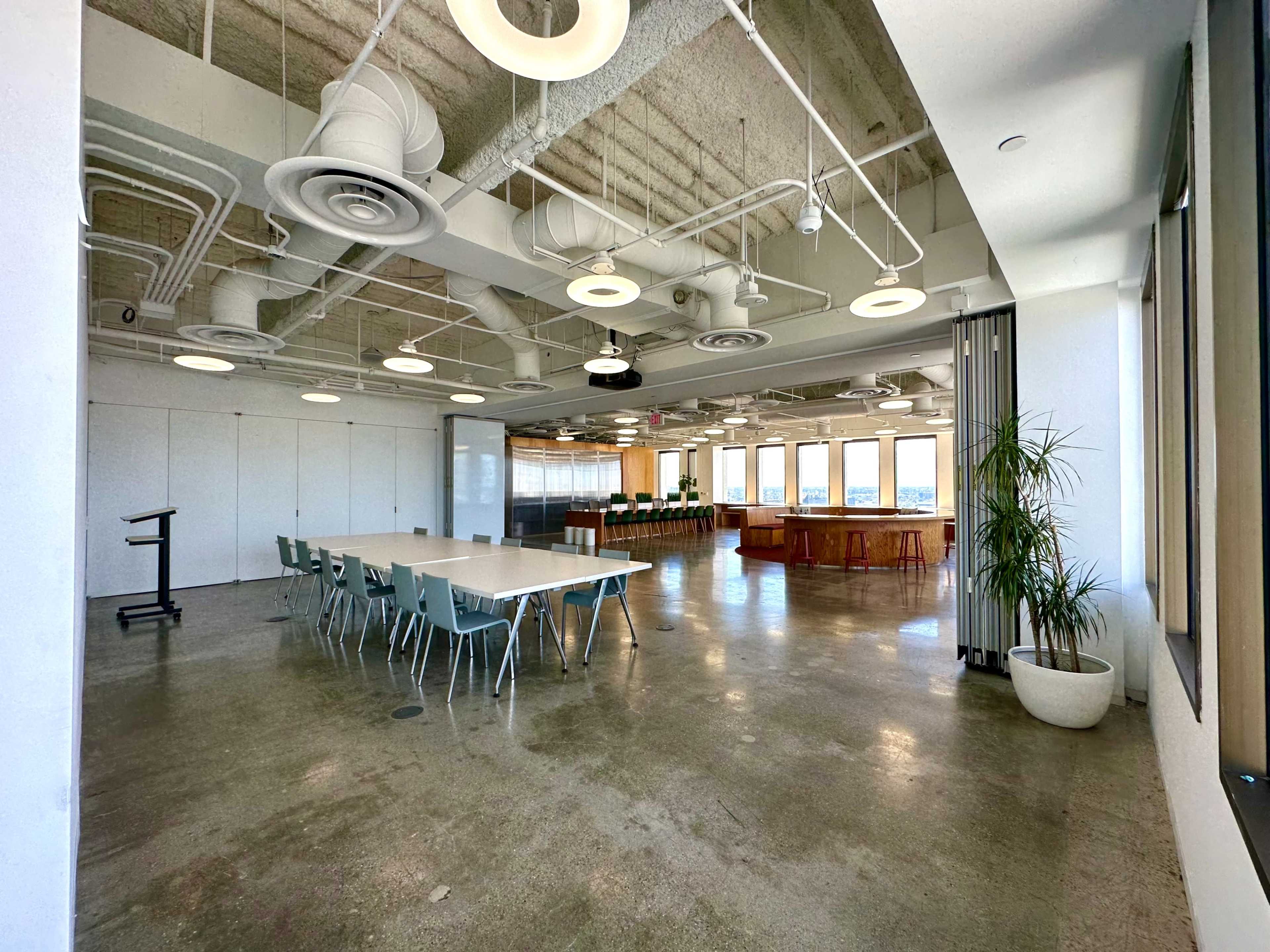 A large, modern conference room features a long table with chairs, a presentation area, and windows offering city views.