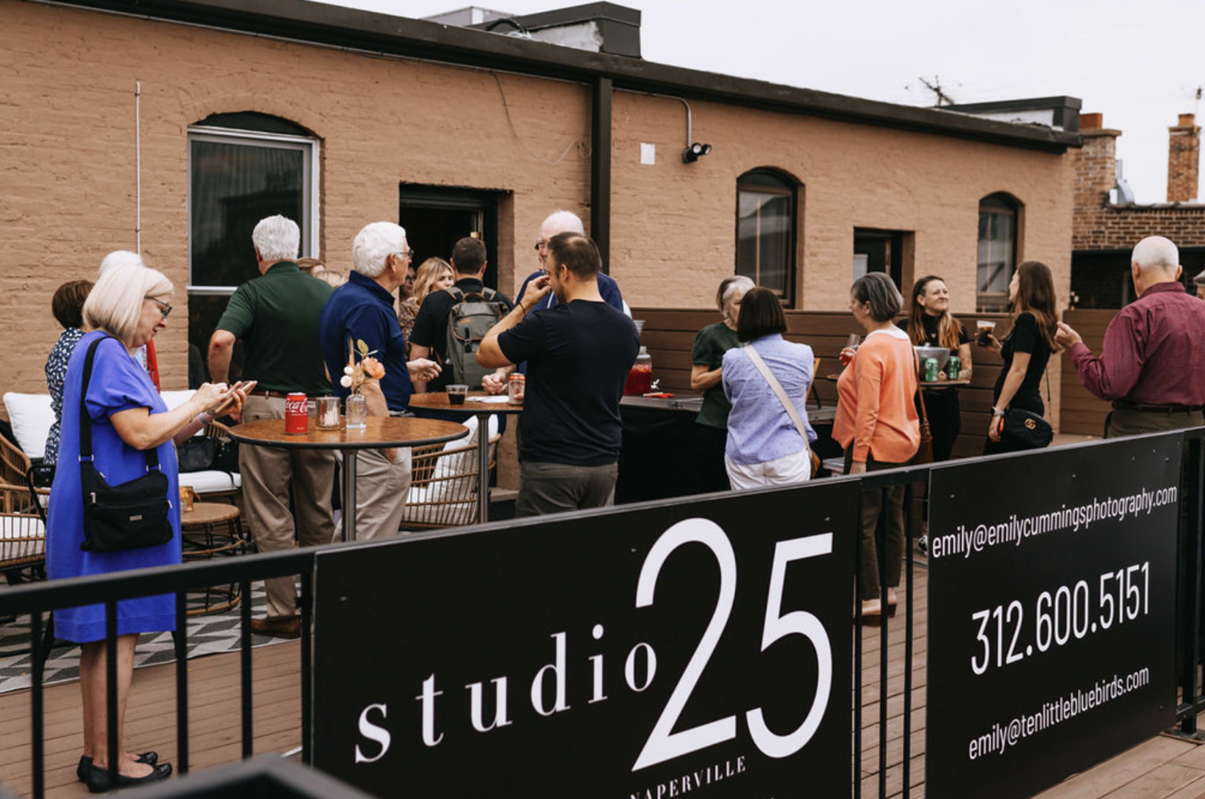A gathering of people socializing on a rooftop deck in front of the studio25 sign in Naperville.