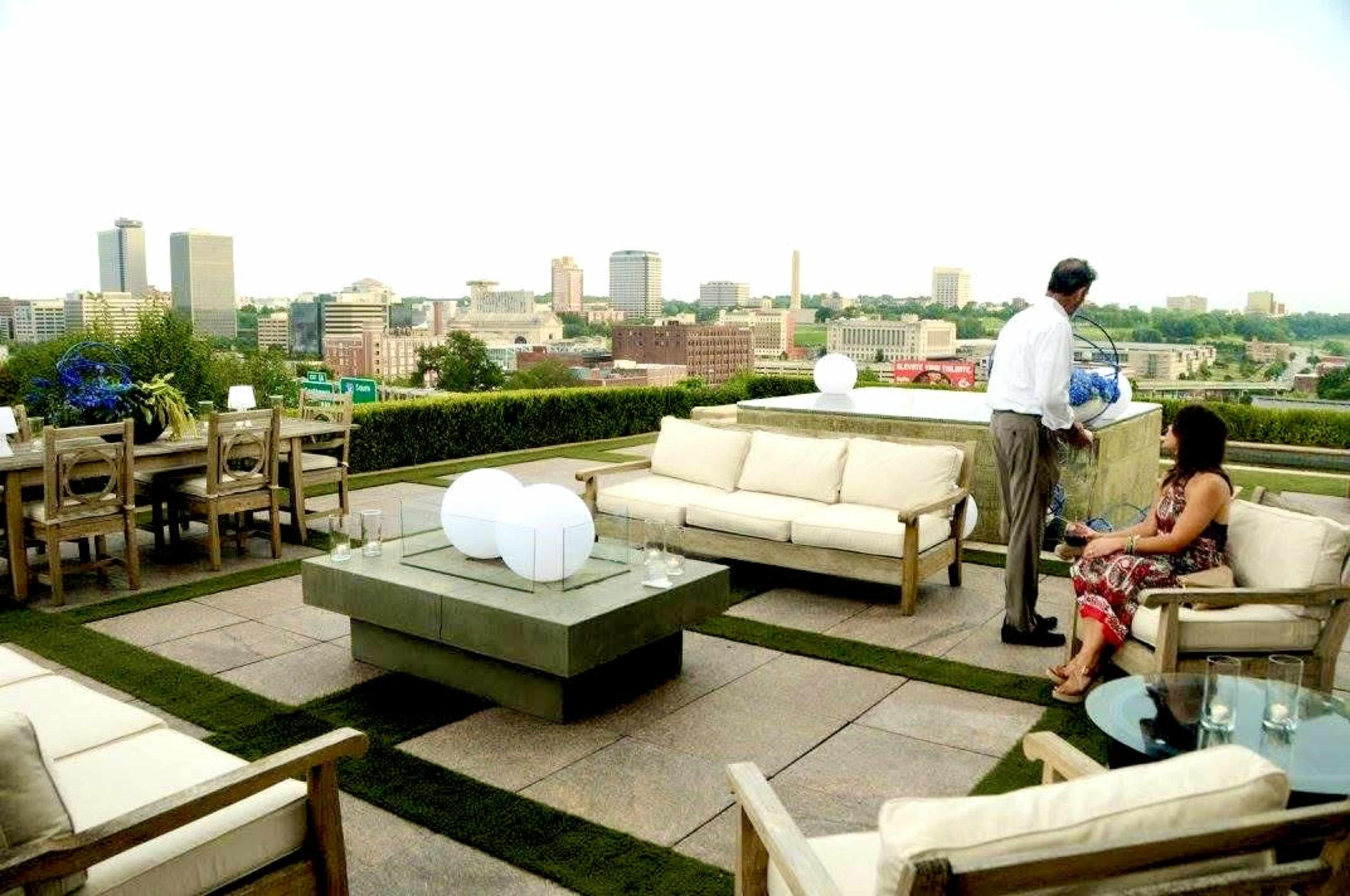 A rooftop terrace features modern furniture, including sofas and a dining area, with a city skyline visible in the background.