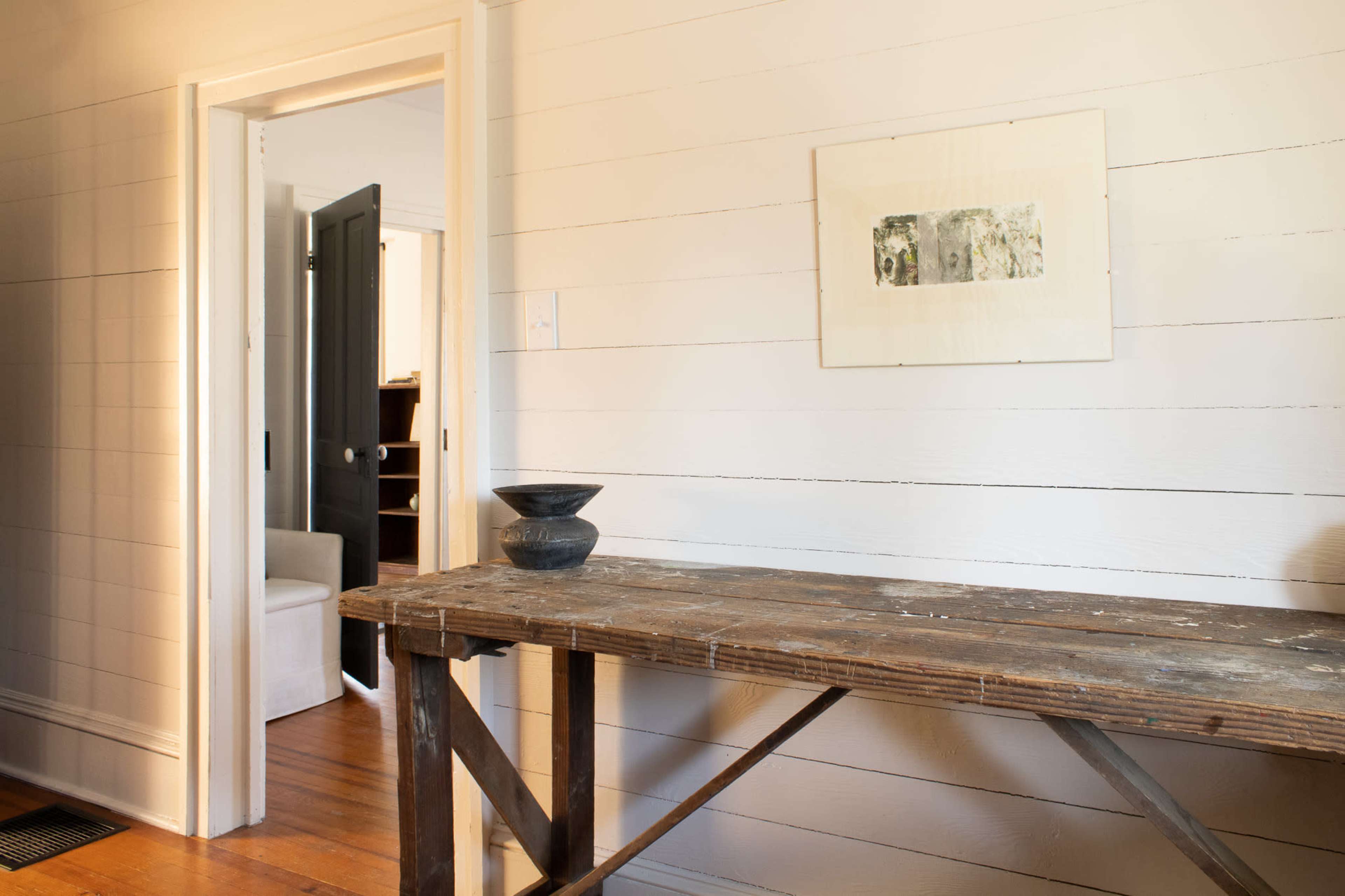 The image shows a wooden table against a white-paneled wall, with a black decorative bowl on it and a doorway leading to another room in the background.