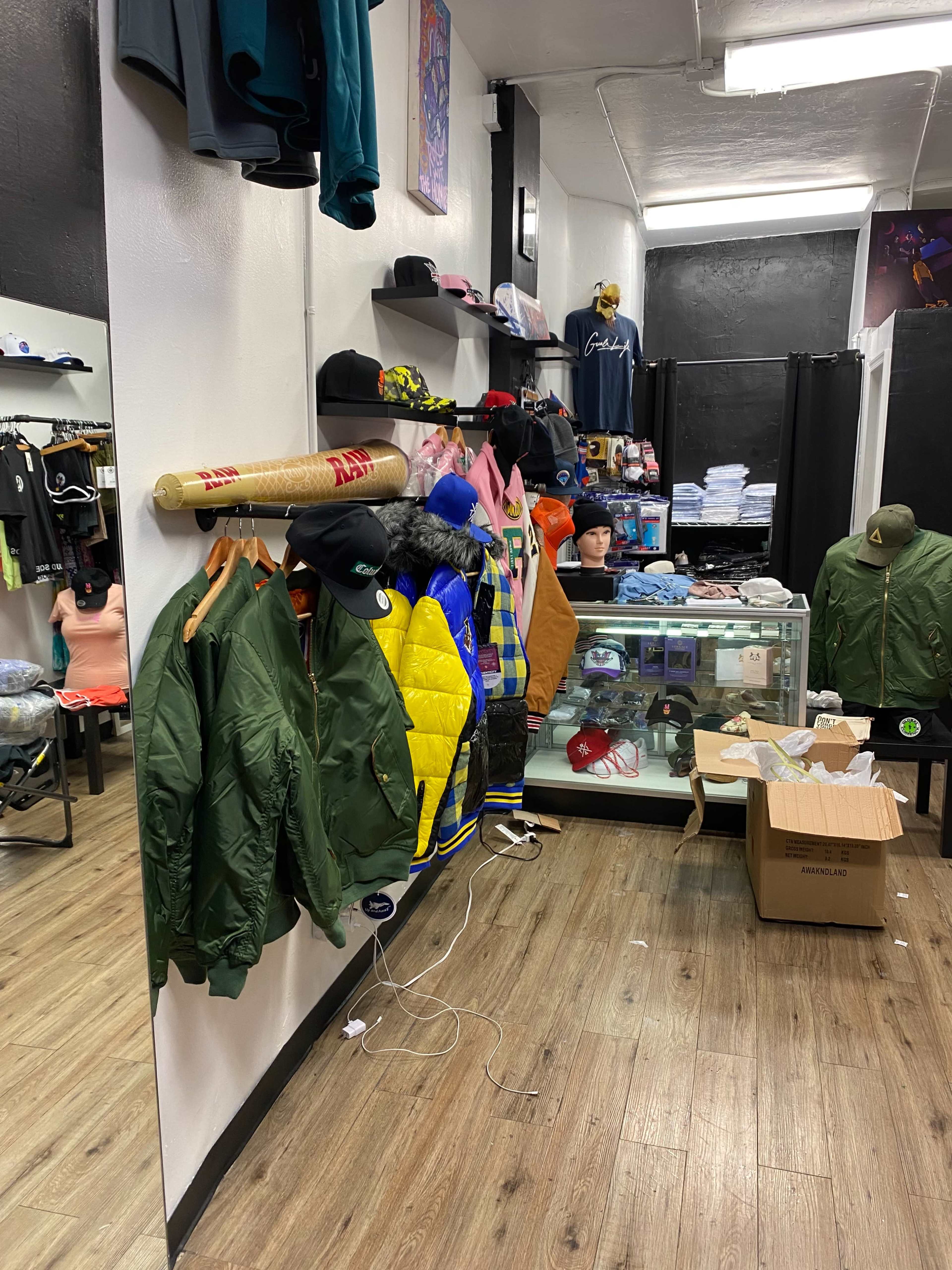 A retail space displaying various clothing items, including jackets hung on a wall, while merchandise is neatly organized on shelves and a glass display case.