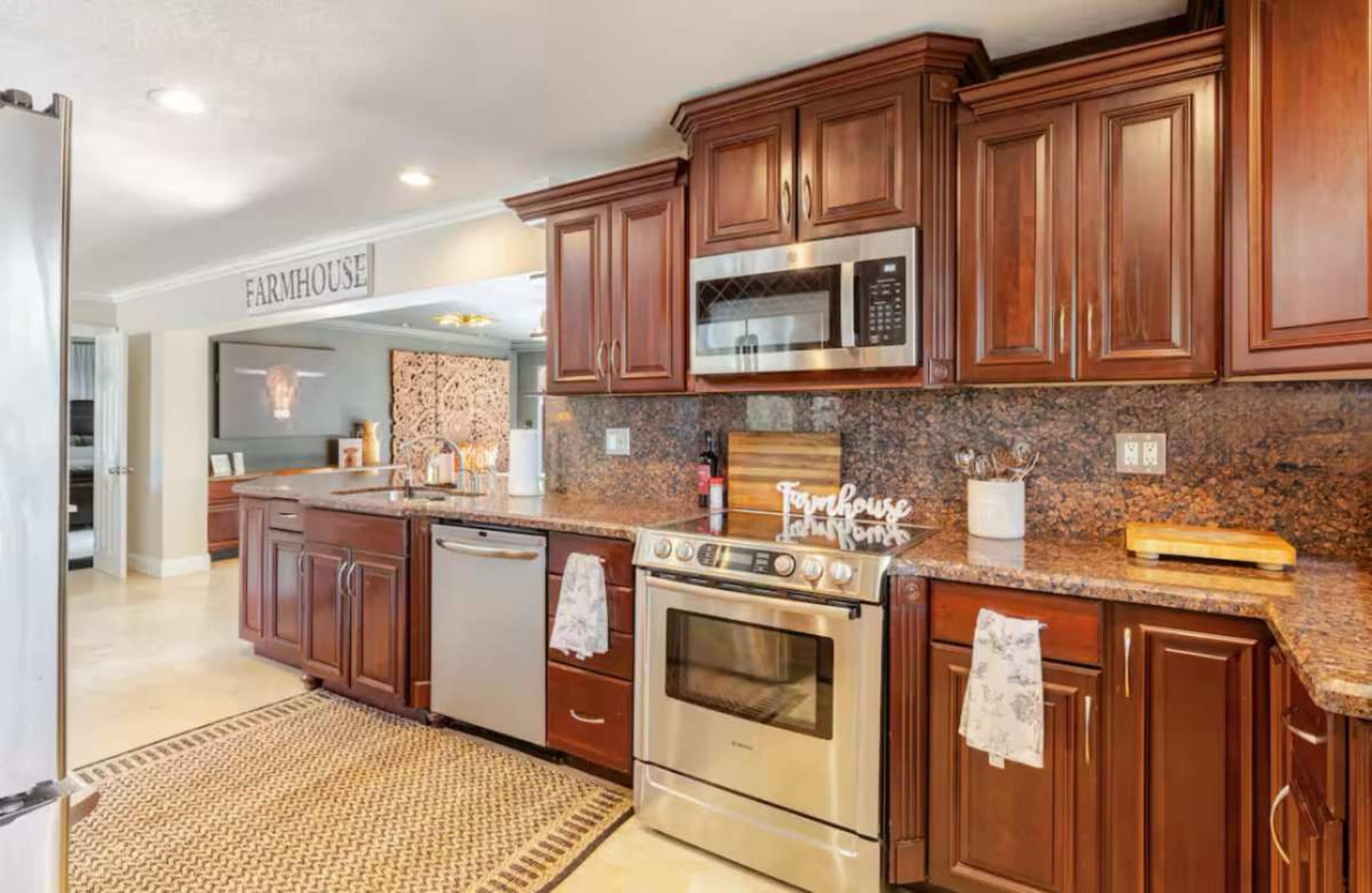 The image shows a modern kitchen featuring dark wooden cabinets, granite countertops, and stainless steel appliances, with a farmhouse-style sign mounted on the wall.