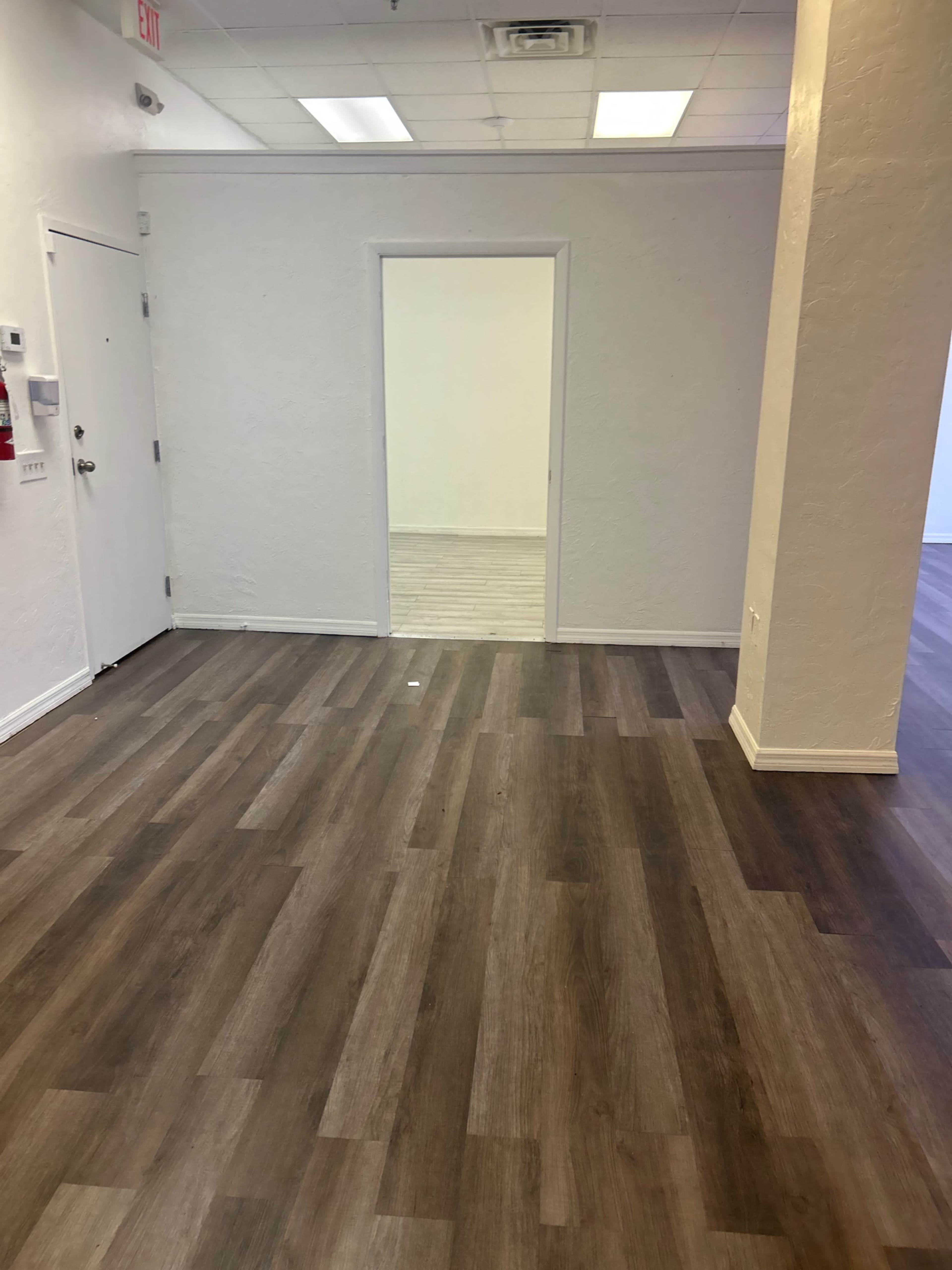 The image shows a spacious interior with light-colored walls and wood-like flooring, featuring an open doorway leading to another room.