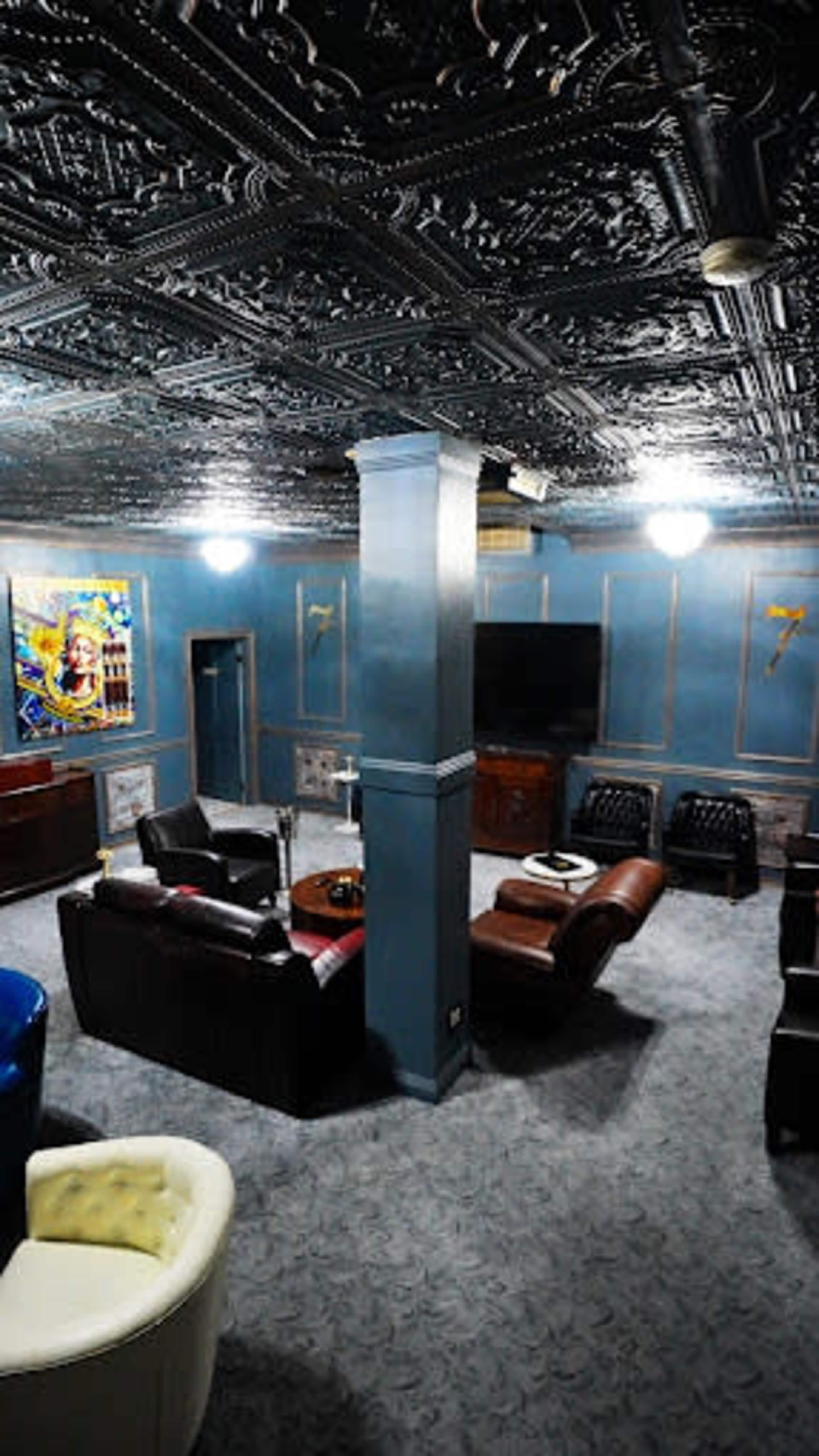 The room features ornate tin ceilings, plush seating arrangements, and a large television against a blue-painted wall.
