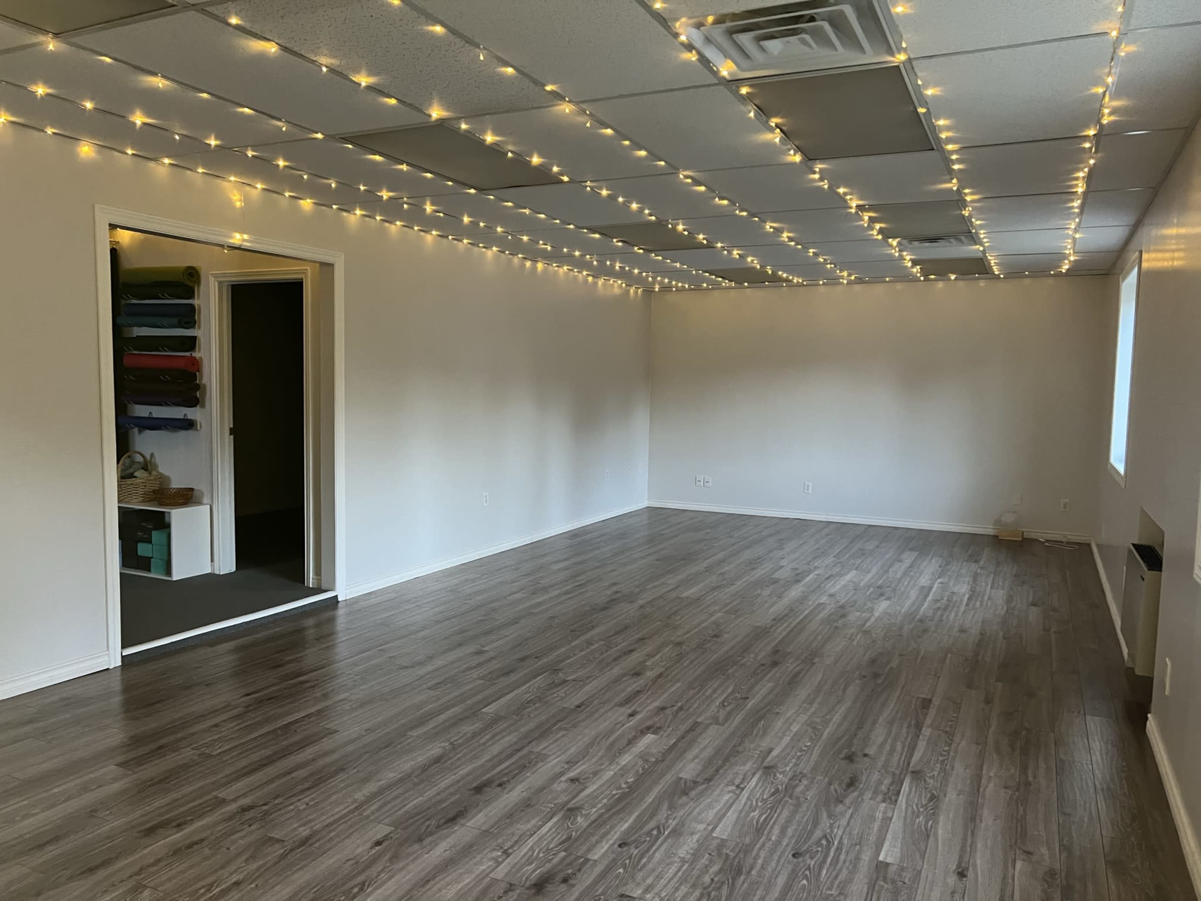 The image shows an empty room with wooden flooring and string lights hanging from the ceiling.