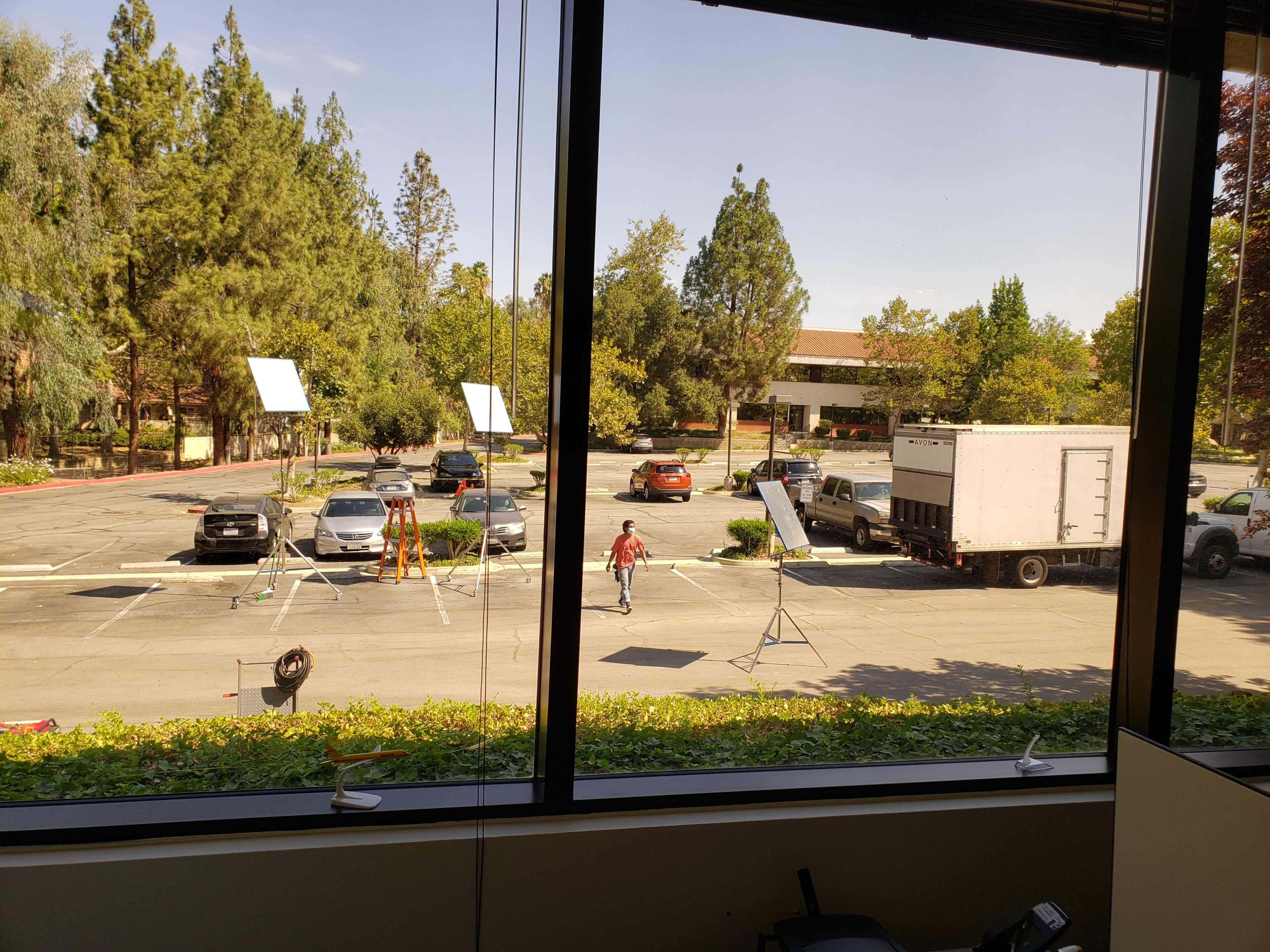 The scene shows a parking lot where several vehicles are parked, along with equipment setups including lights and tripods.