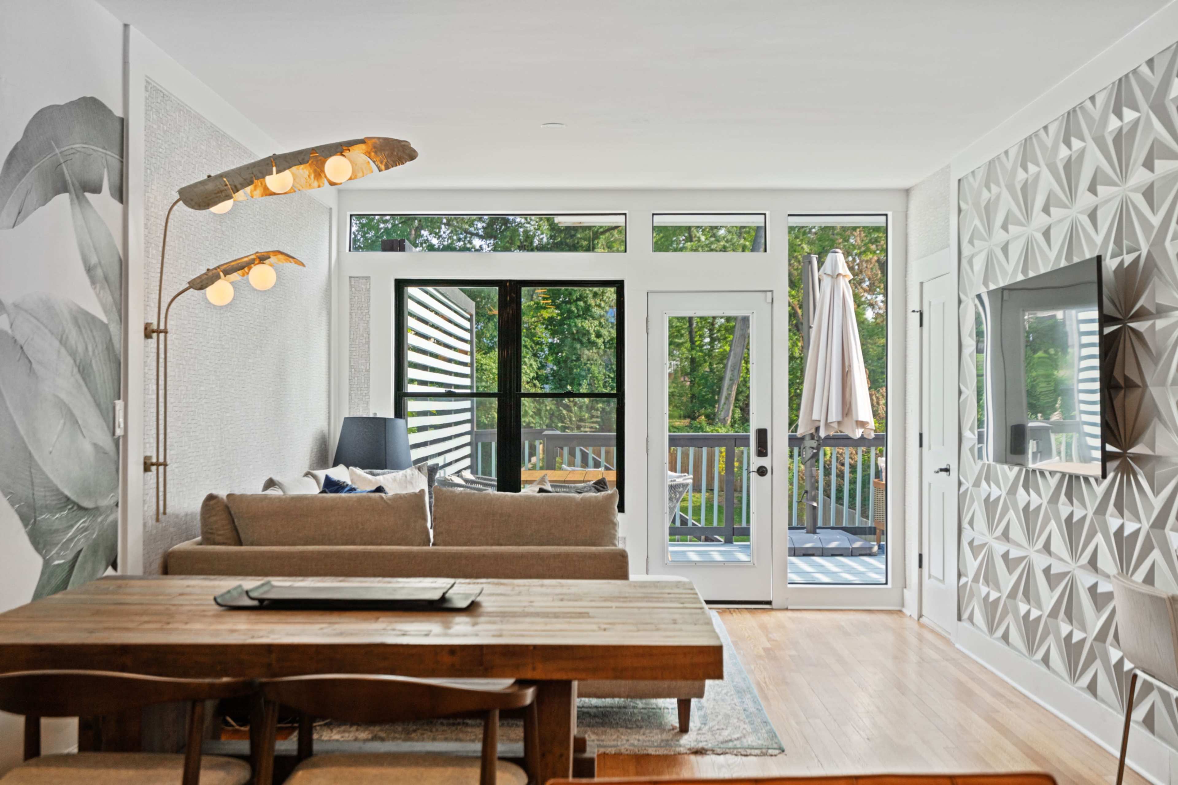 A stylish living area features a sofa and a wooden dining table, with large windows that open to a deck.
