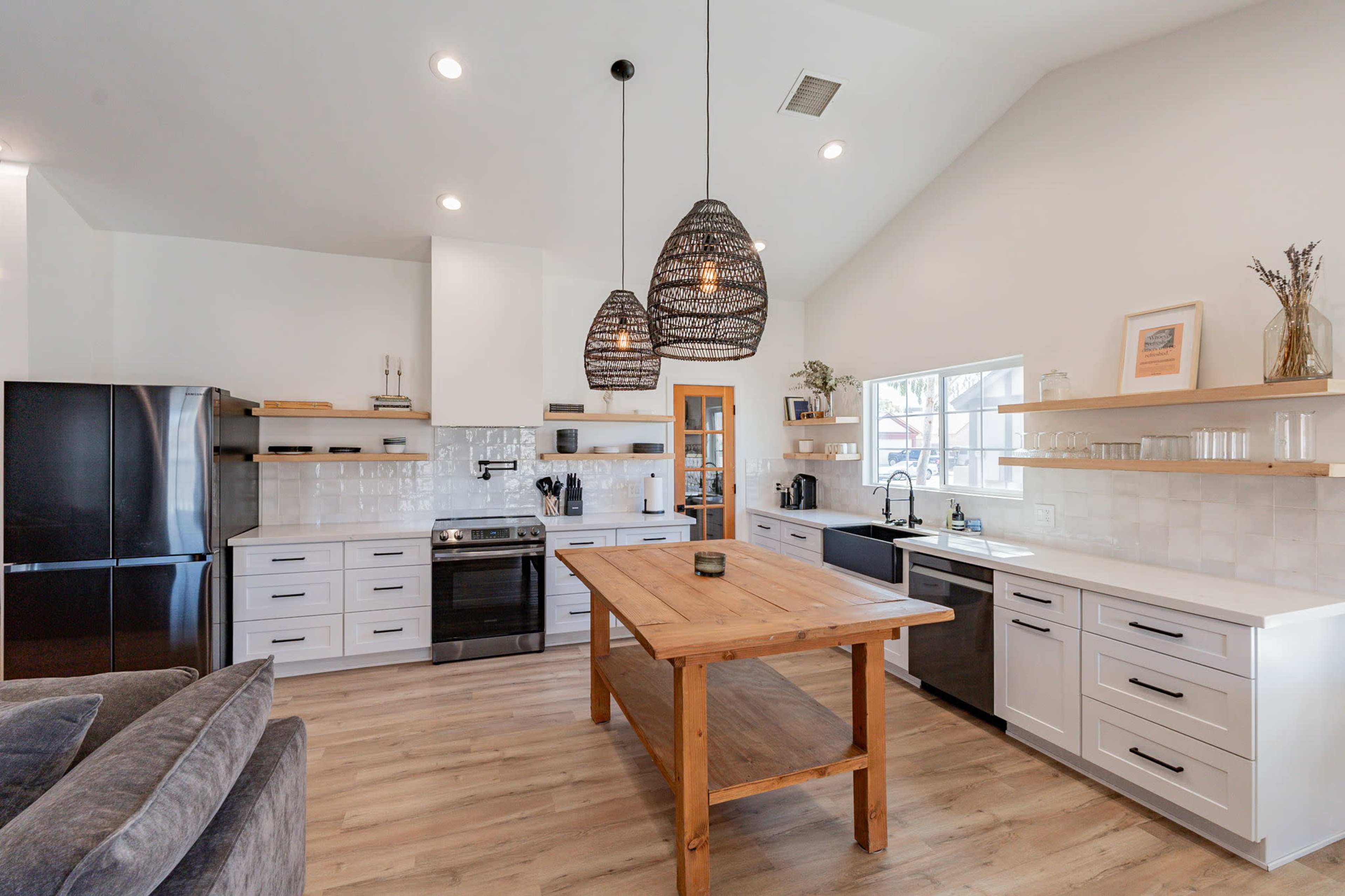 The image shows a modern kitchen featuring white cabinetry, a large wooden island, and pendant lights hanging from the ceiling.