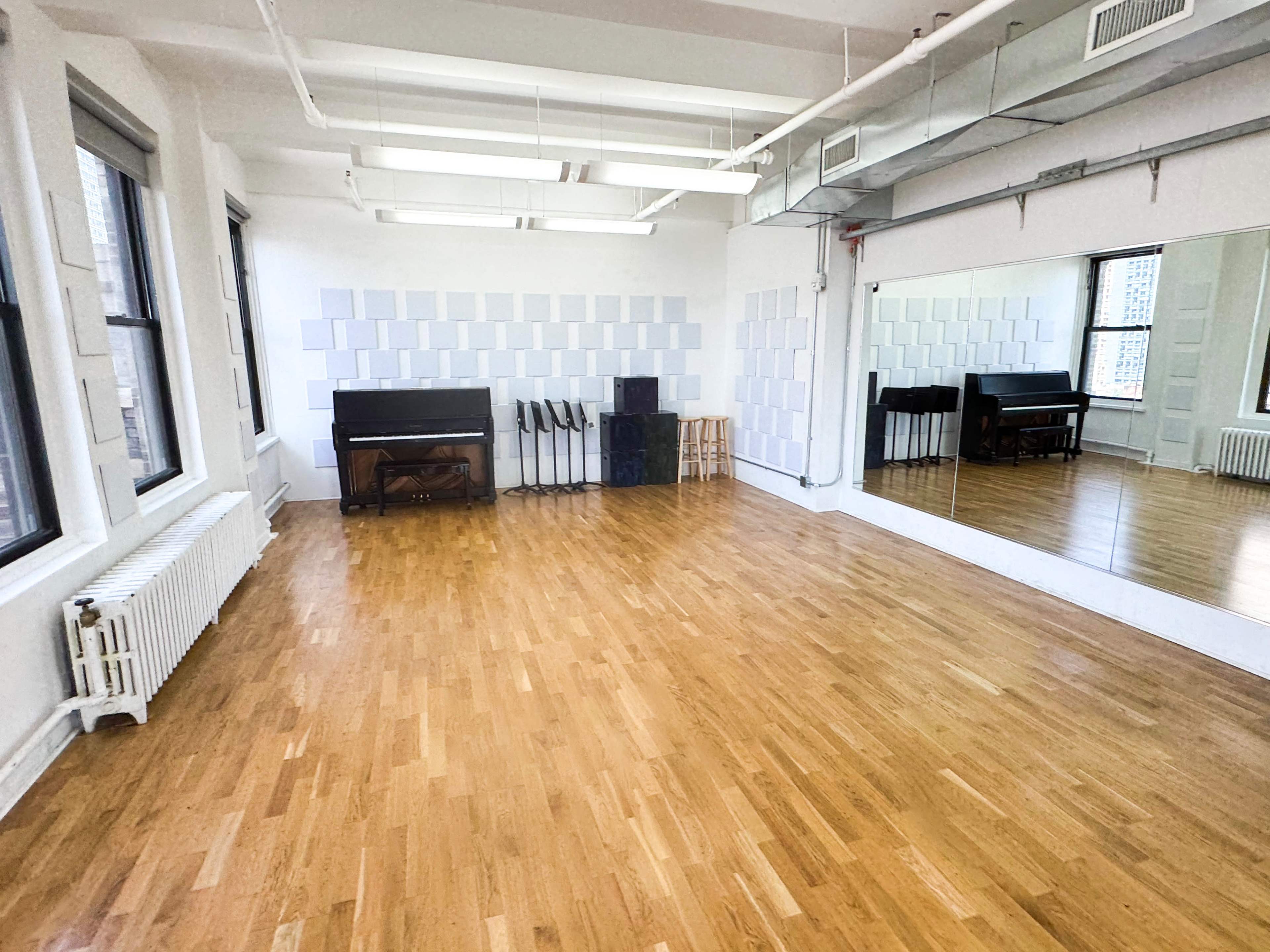 A spacious room with wooden flooring, a black piano, and a large mirror along one wall.