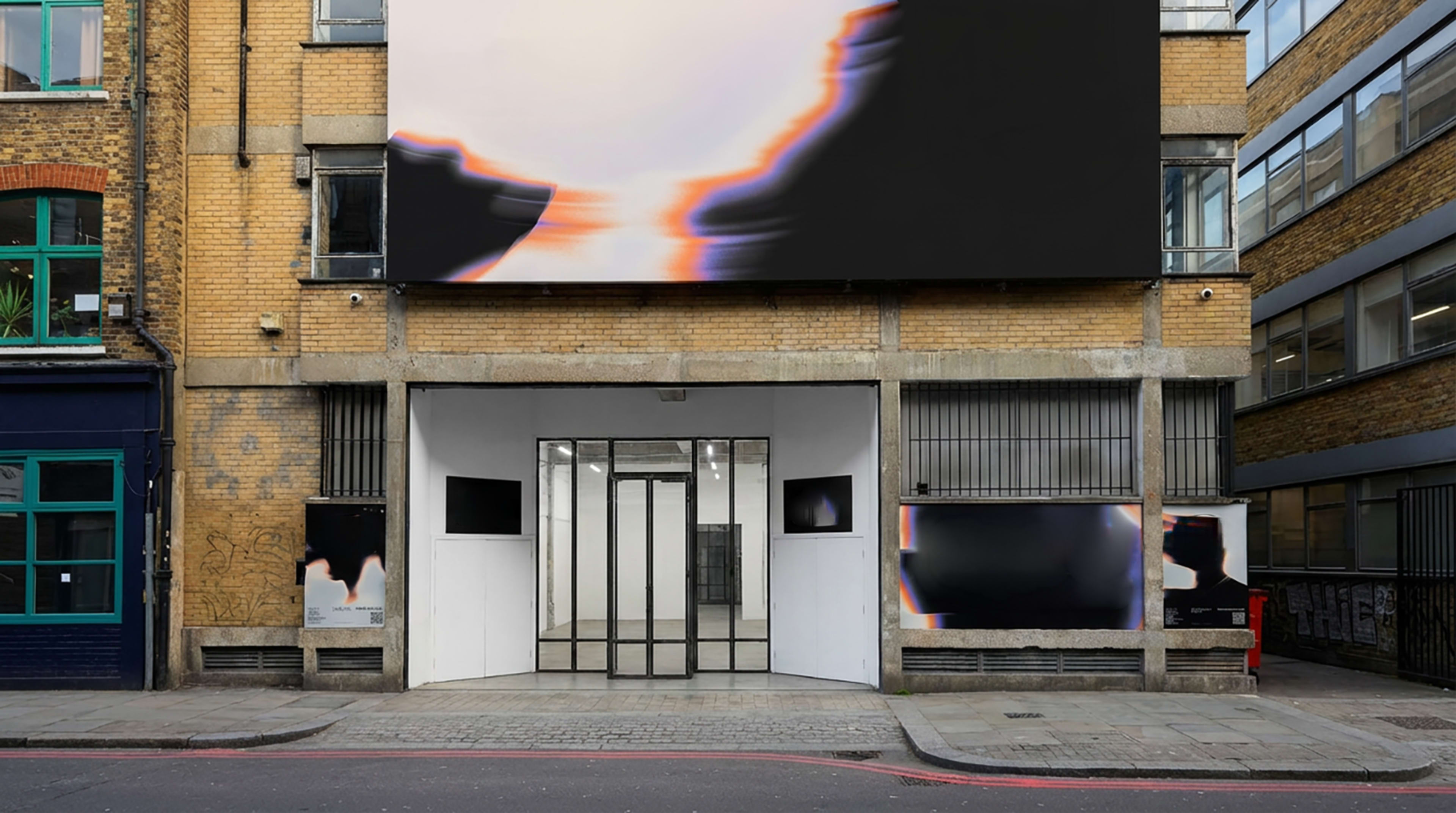 The image shows a modern building facade with large digital screens and a glass entrance, located on a city street.