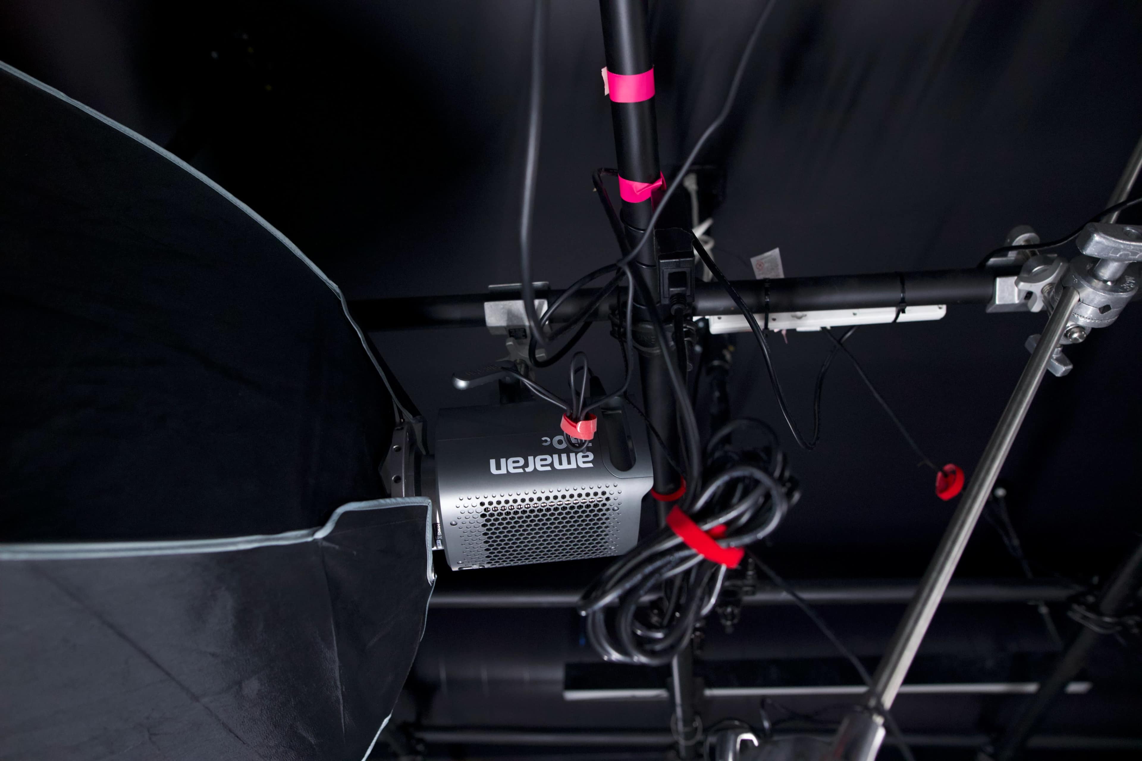 The image shows a ceiling-mounted projector with various cables and a light modifier attached.