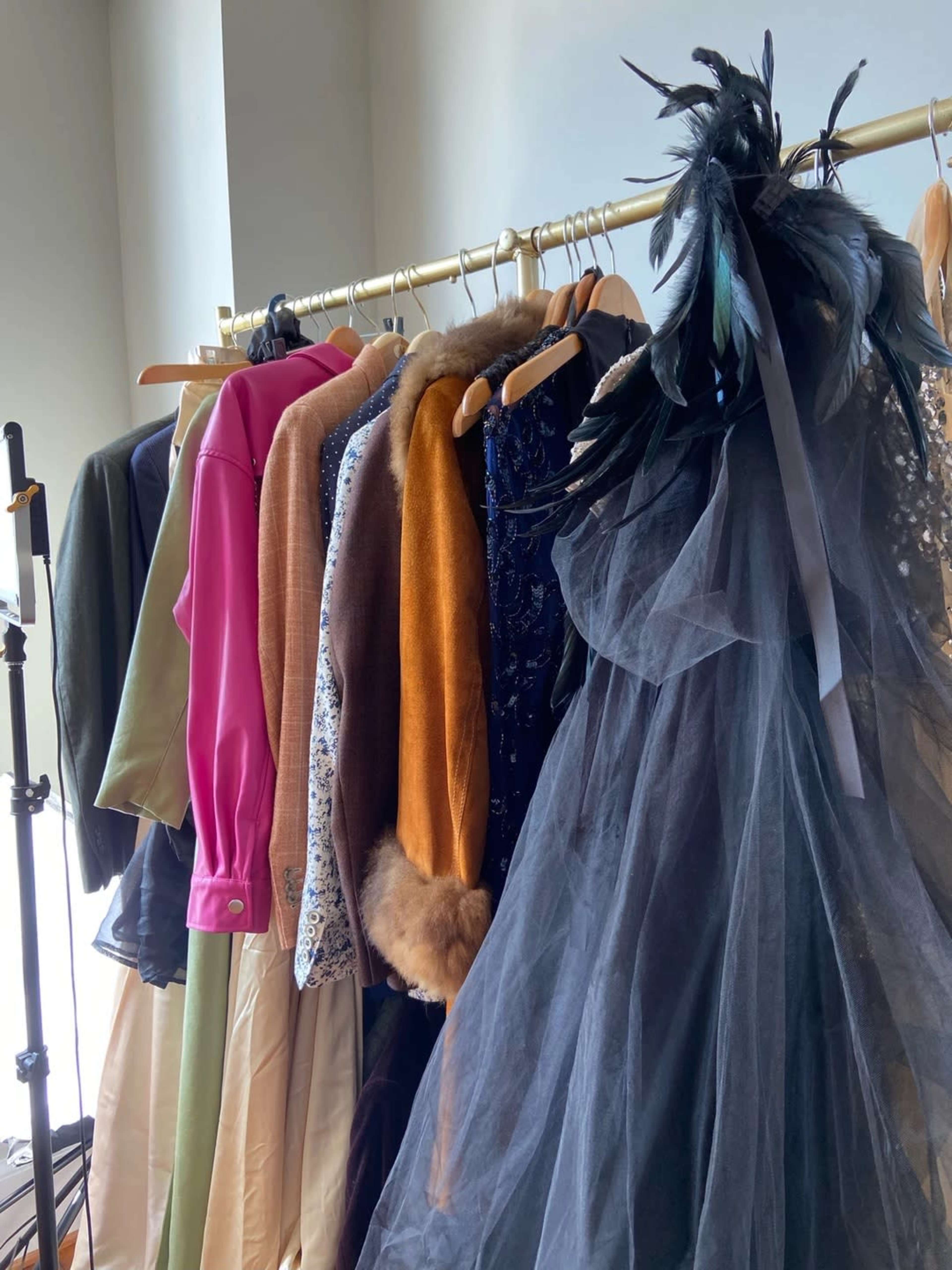 A rack of clothing holds various garments, including a black tulle dress, coats, and brightly colored tops.