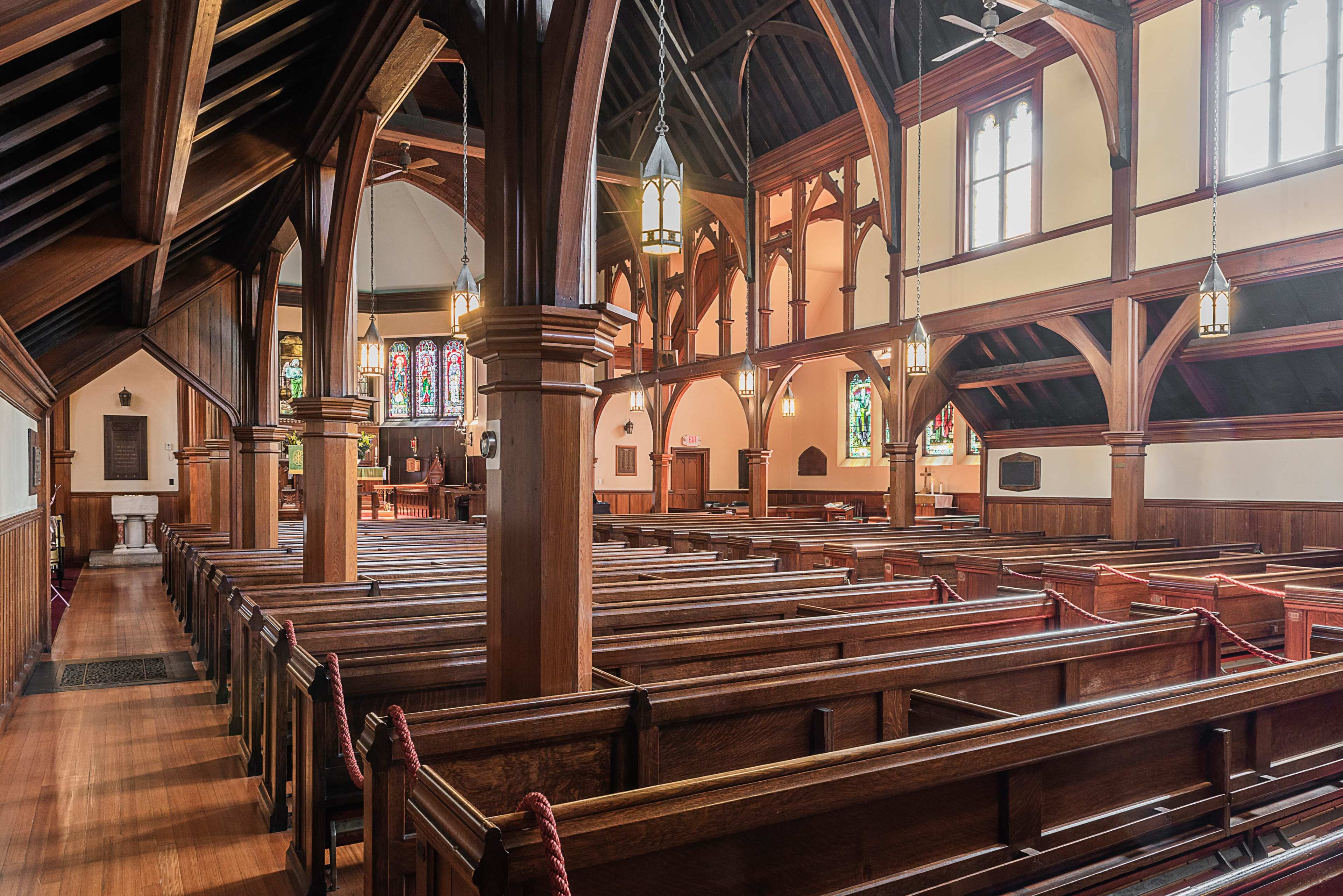 The interior of a wooden church with rows of pews and stained glass windows.