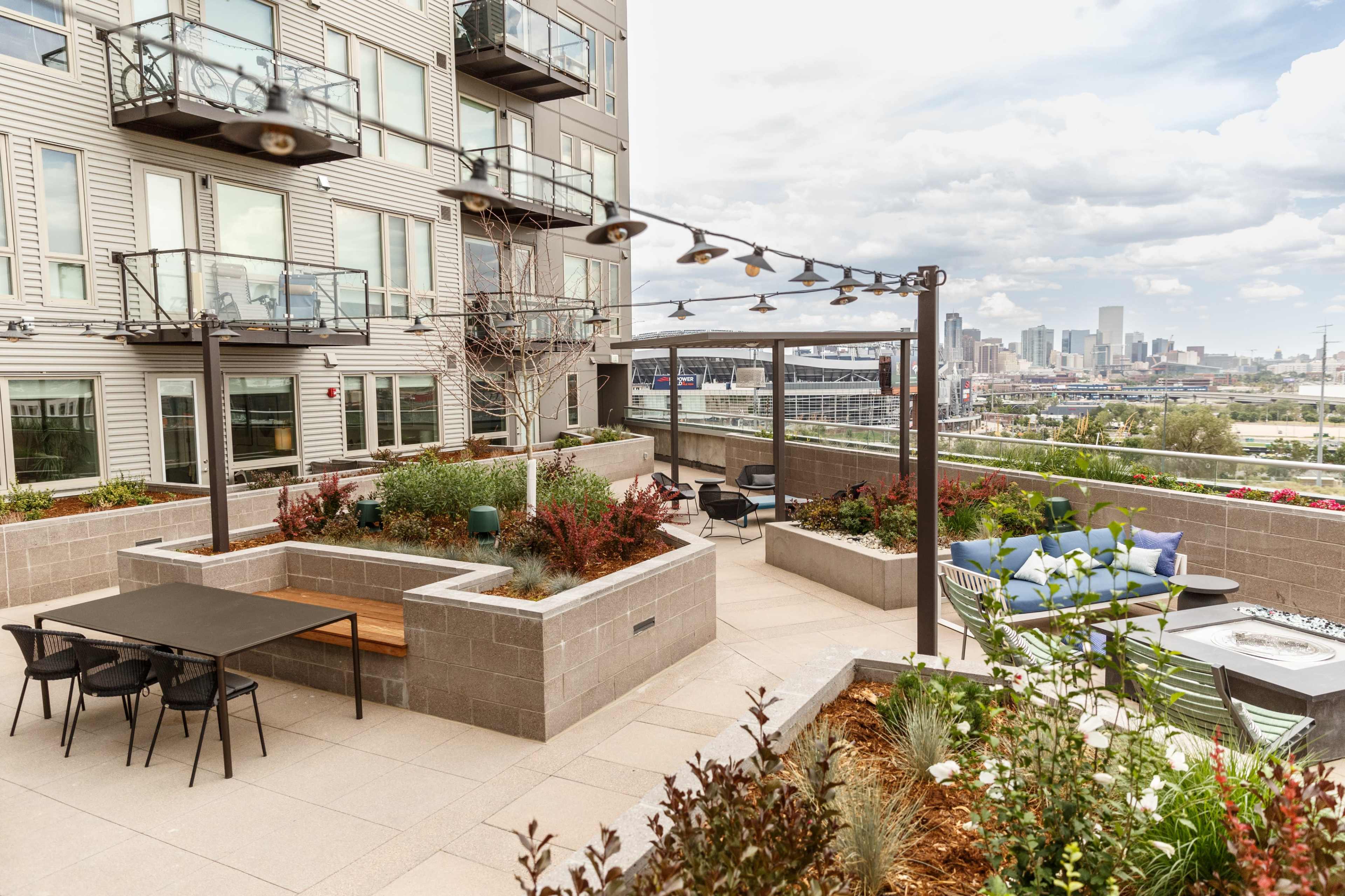 The image shows a multi-level outdoor terrace with planters, seating areas, and a skyline view in the background.