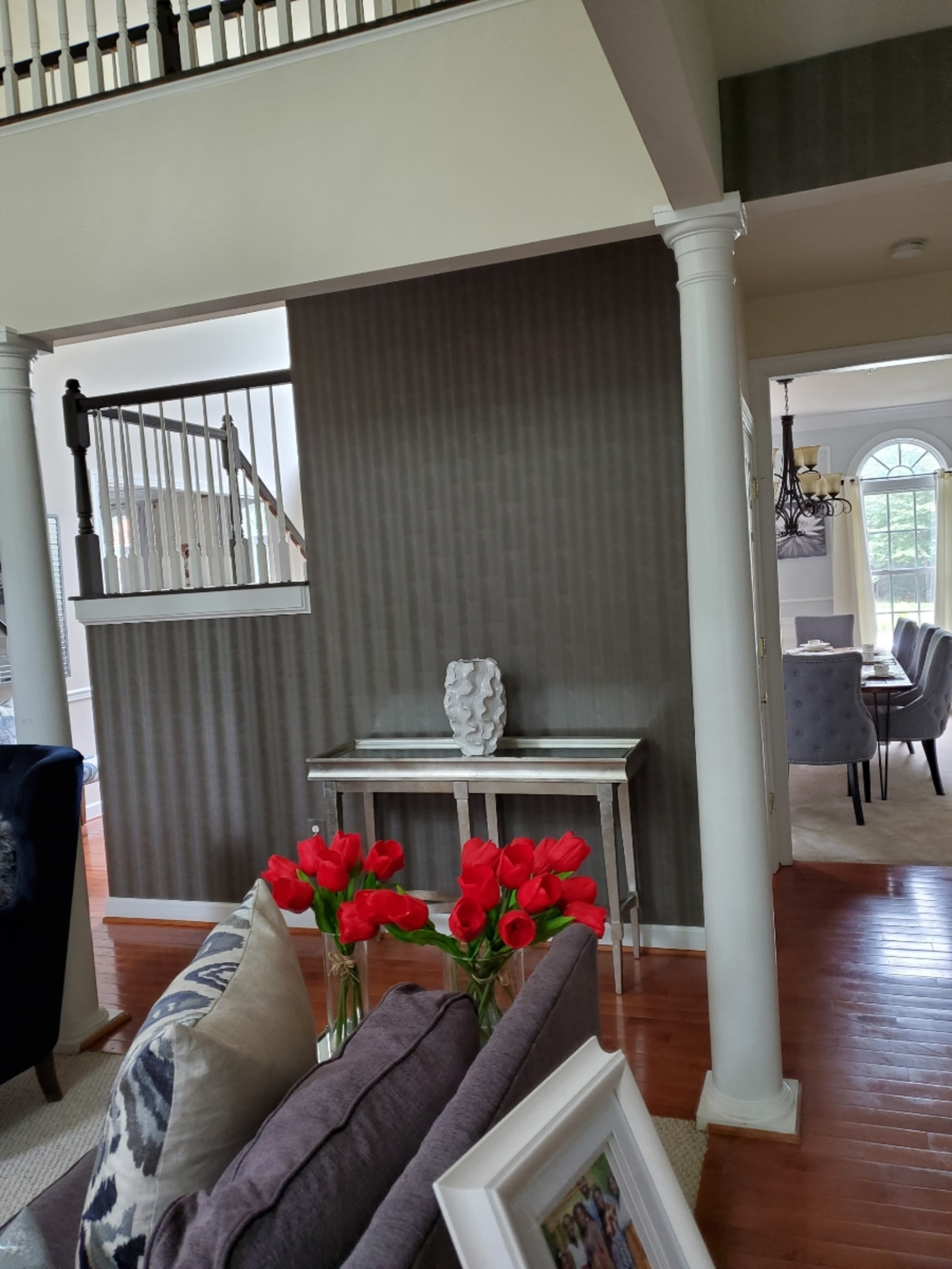 A living room with a console table and a vase of red tulips against a striped wallpaper backdrop, framed by two white columns.