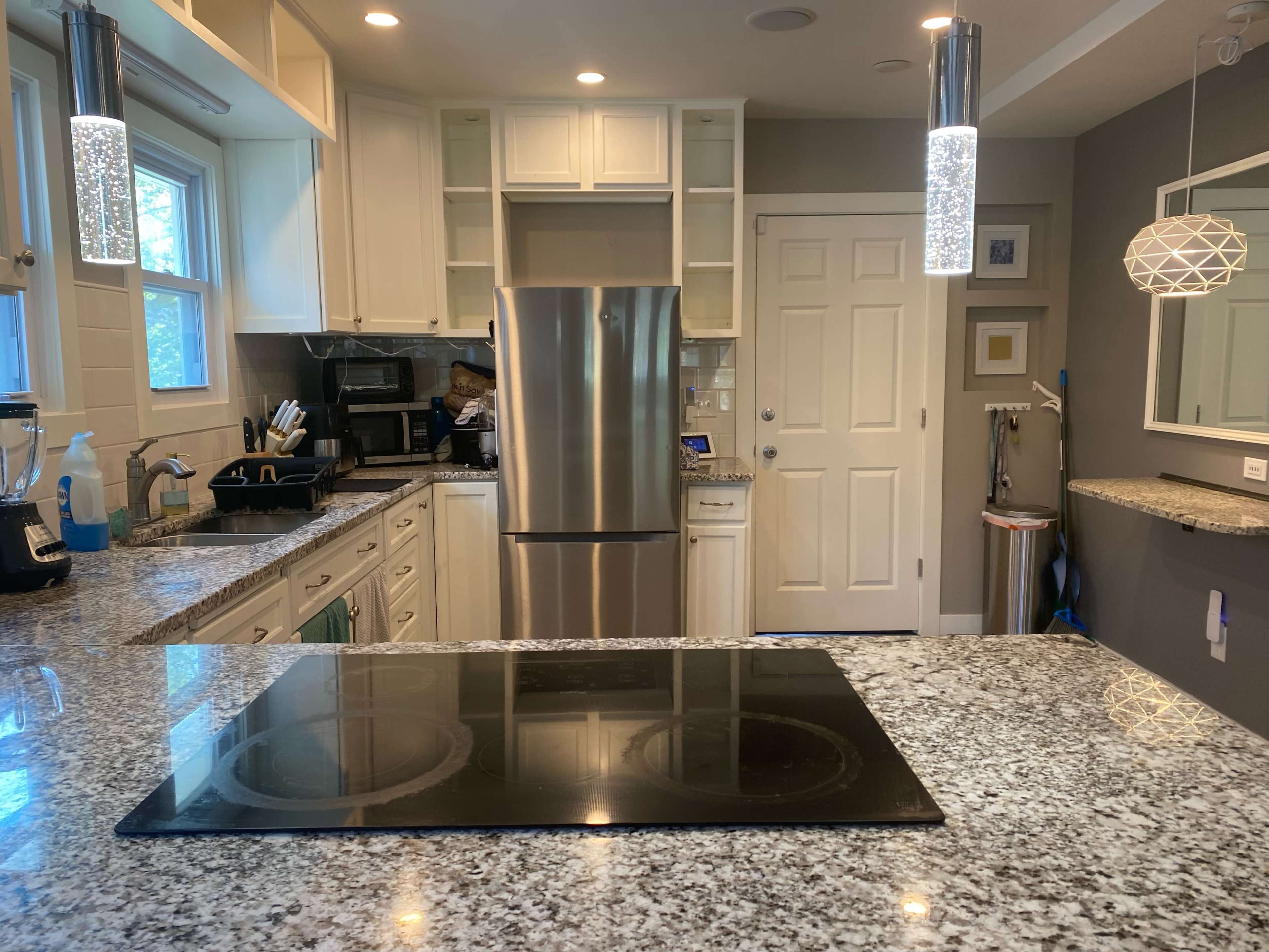 A modern kitchen features stainless steel appliances, a granite countertop with a cooktop, and light-colored cabinetry.