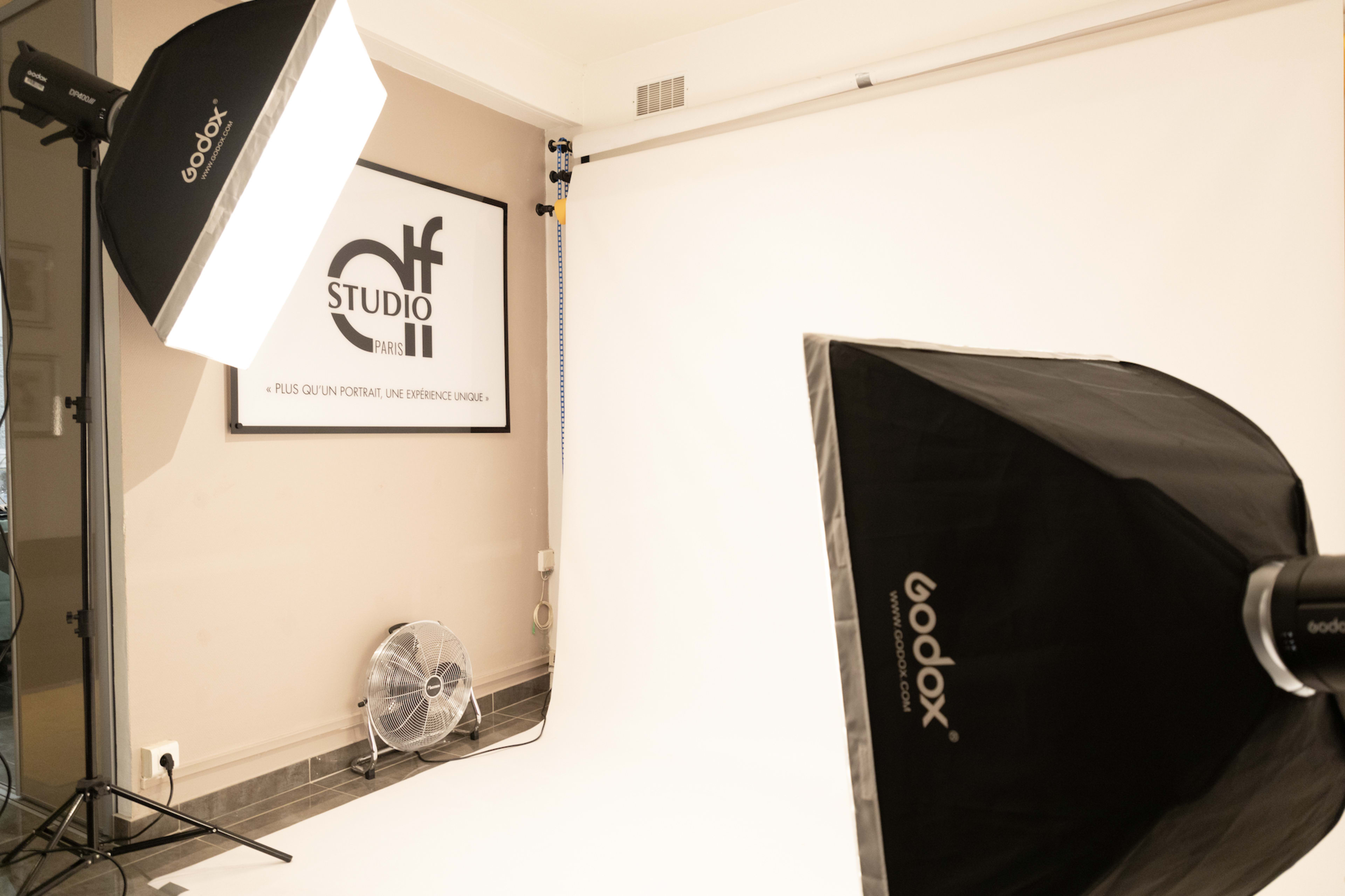 A photography studio setting with two softbox lights, a fan, and a blank backdrop.