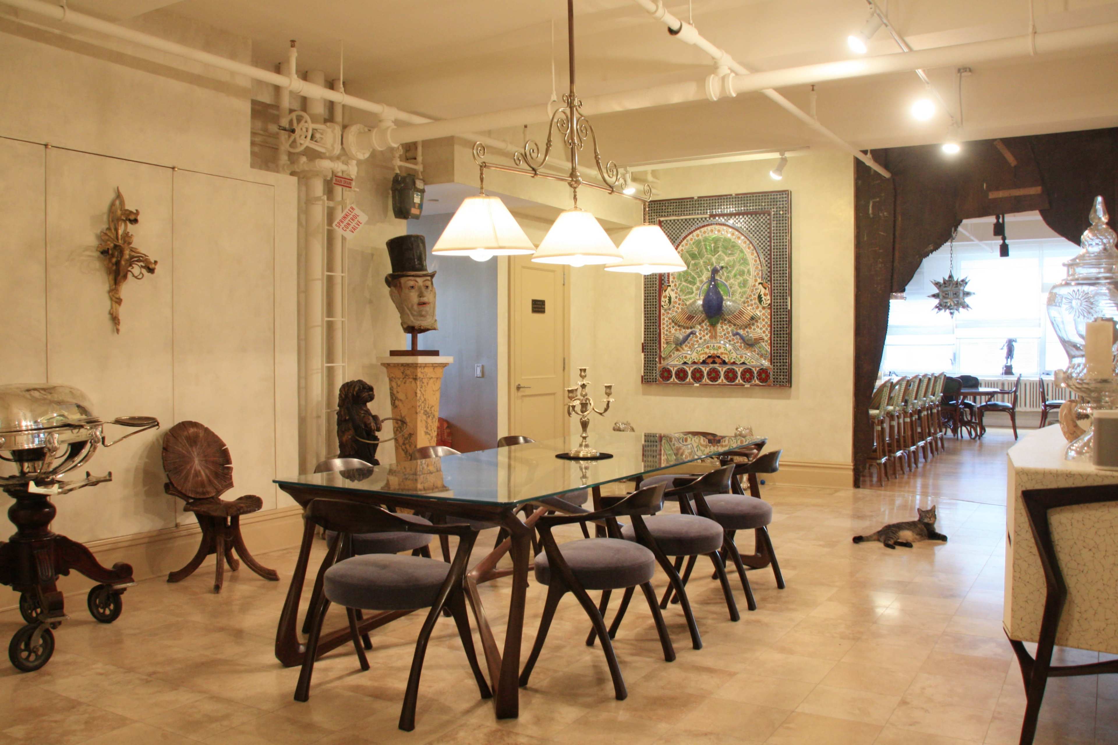 The image shows a spacious dining area with a glass-top table surrounded by upholstered chairs, ornate artwork on the walls, and various decorative items throughout the room.