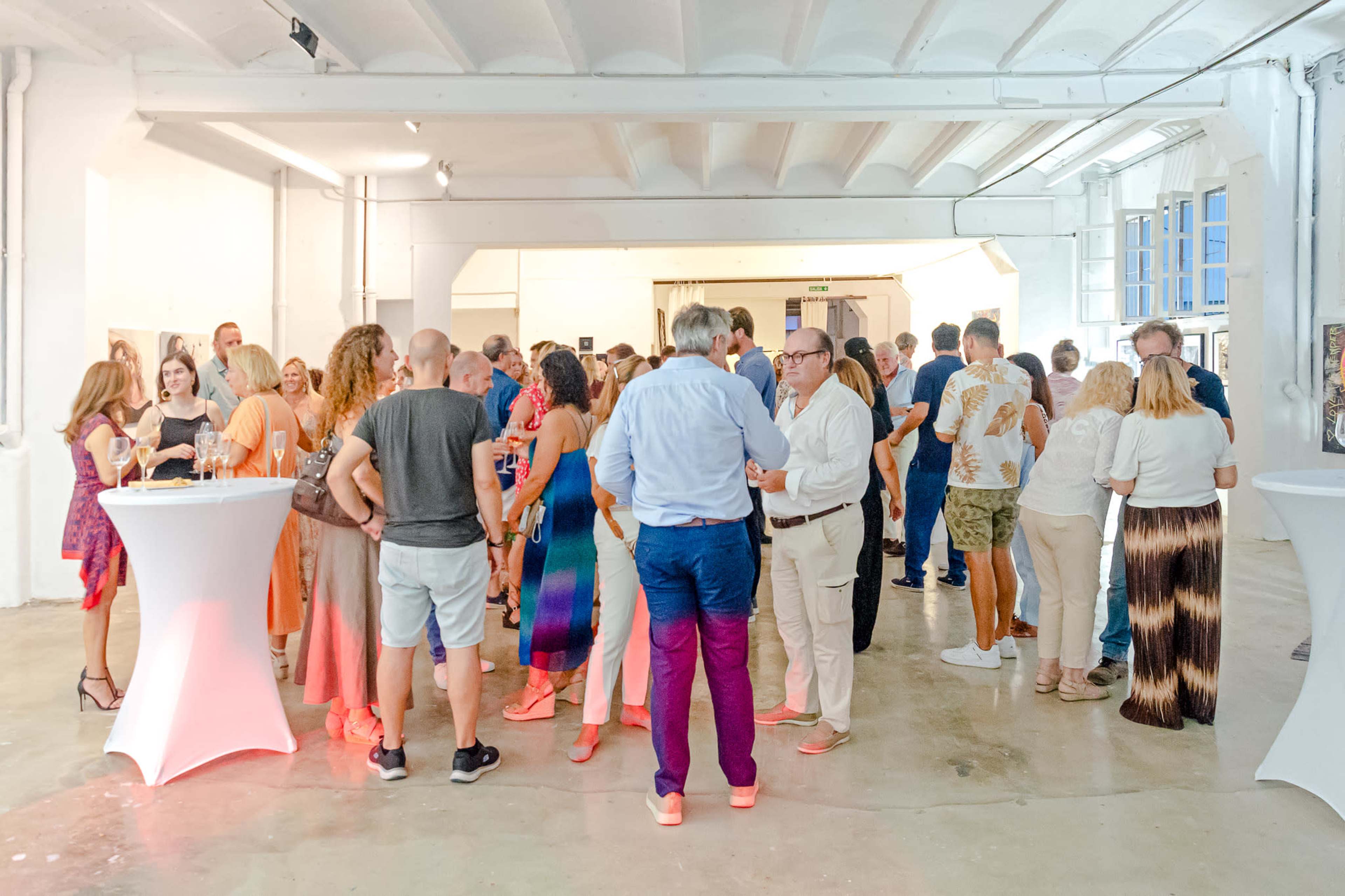 A large group of people mingles at a social event in a spacious, brightly lit gallery with modern decor.
