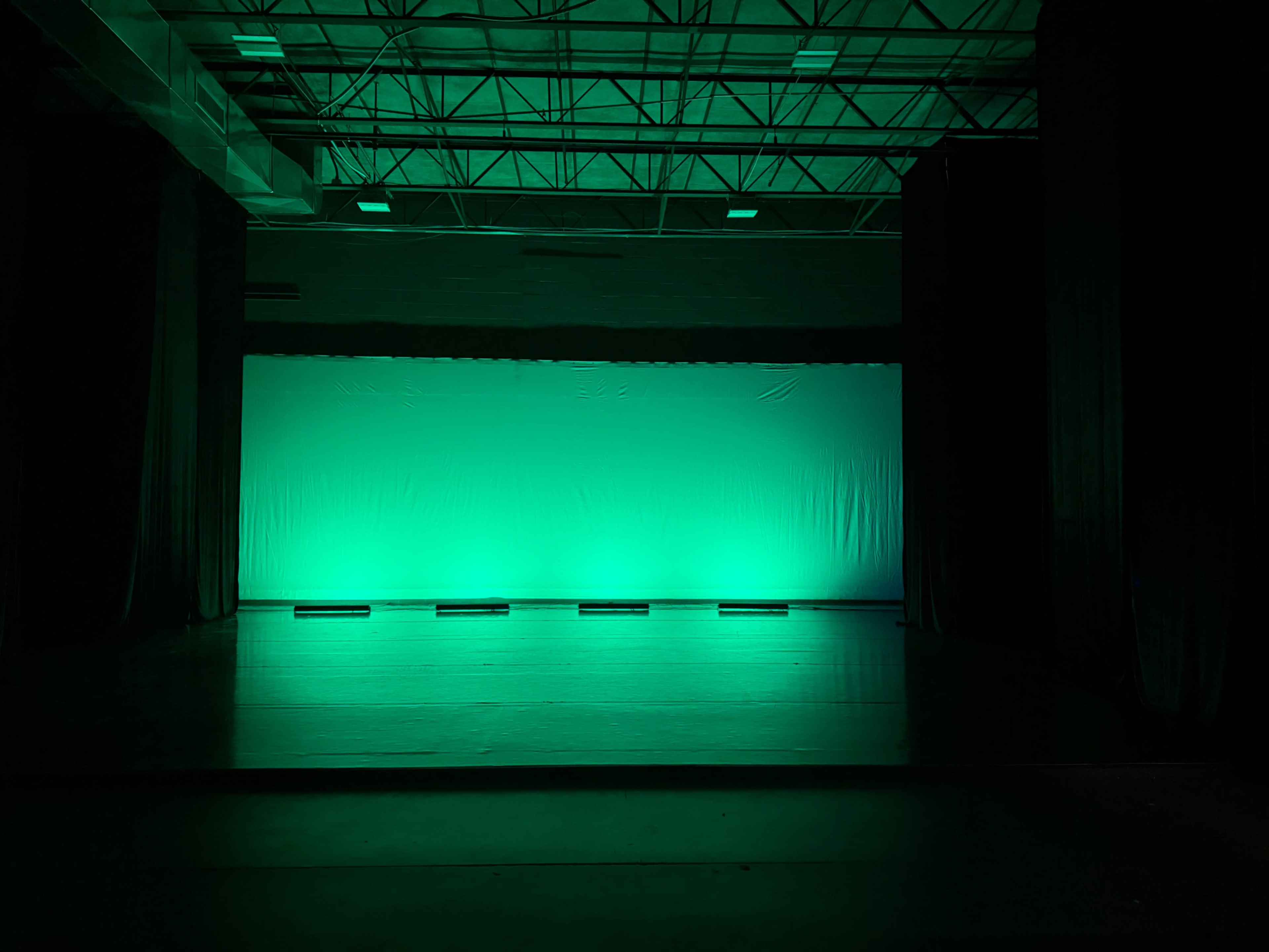 The image shows a dimly lit stage with a bright green backdrop and a darkened surrounding area.