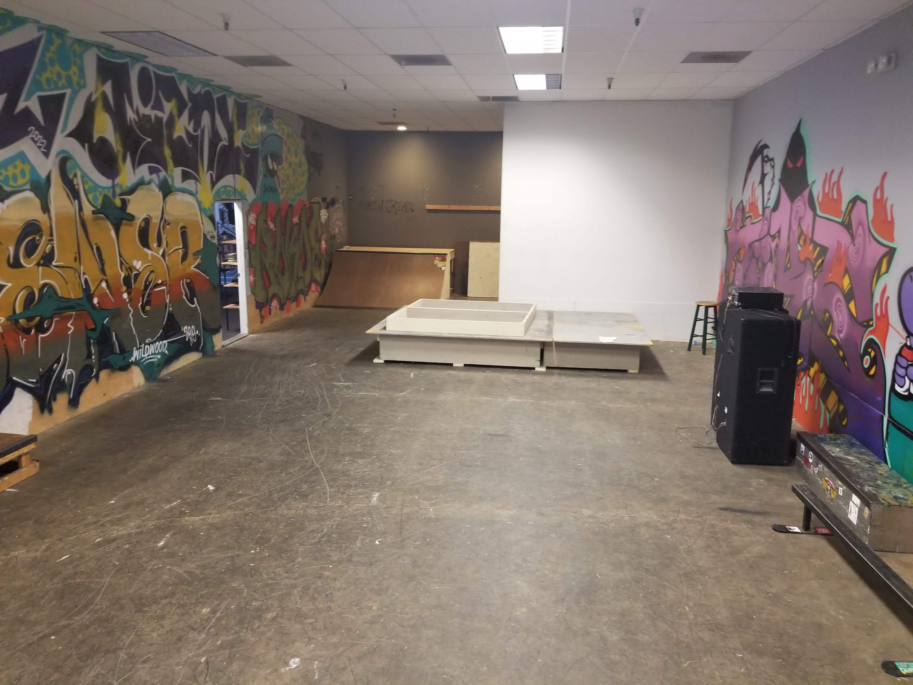 An indoor skate park with graffiti-covered walls, a rectangular wooden ramp, and some skateboarding equipment.