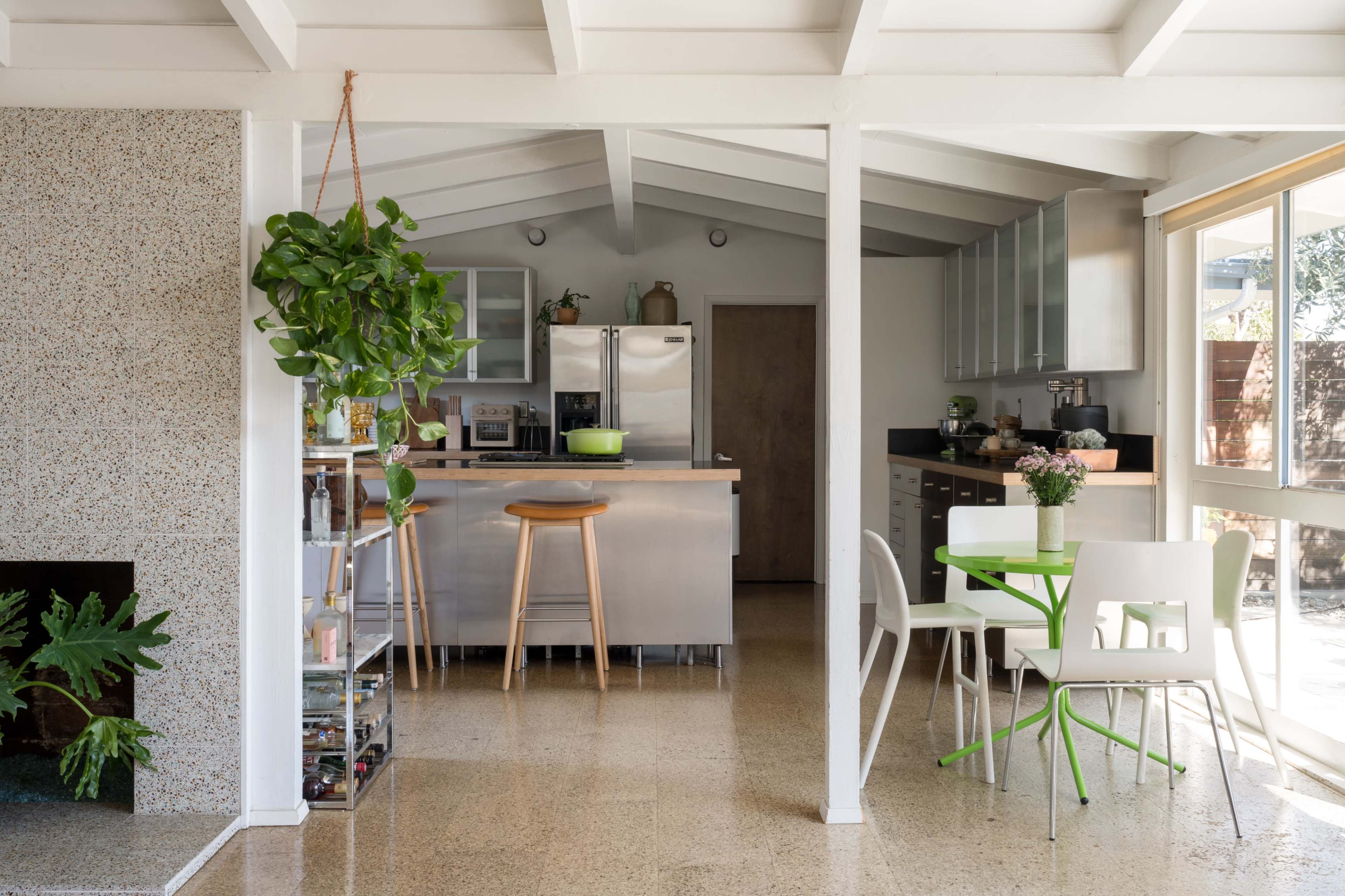 The image shows a modern kitchen with stainless steel appliances, a large island with bar stools, and a dining table set near a wall of windows.