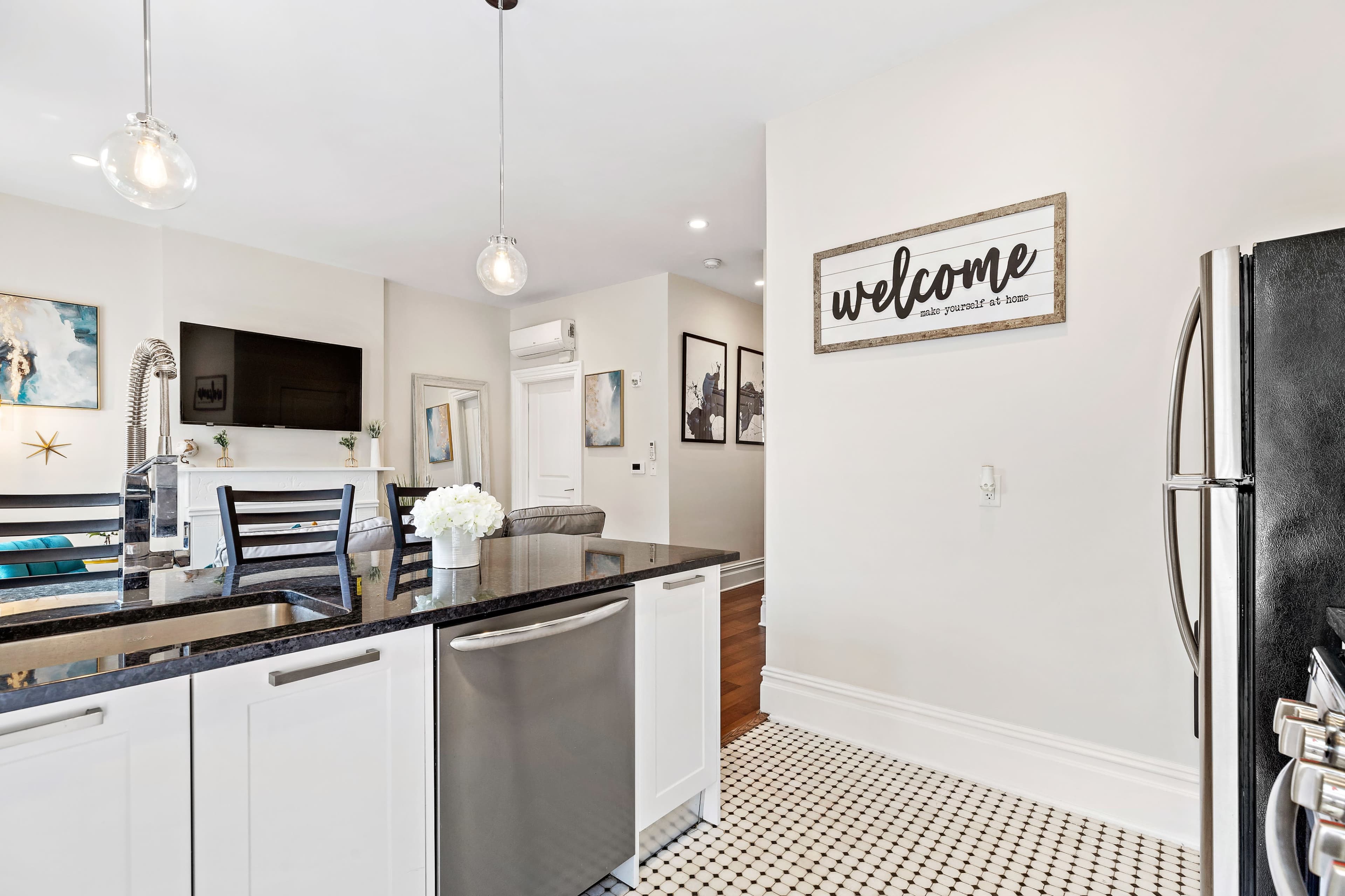 A modern kitchen with black countertops, stainless steel appliances, and a decorative "welcome" sign on the wall.