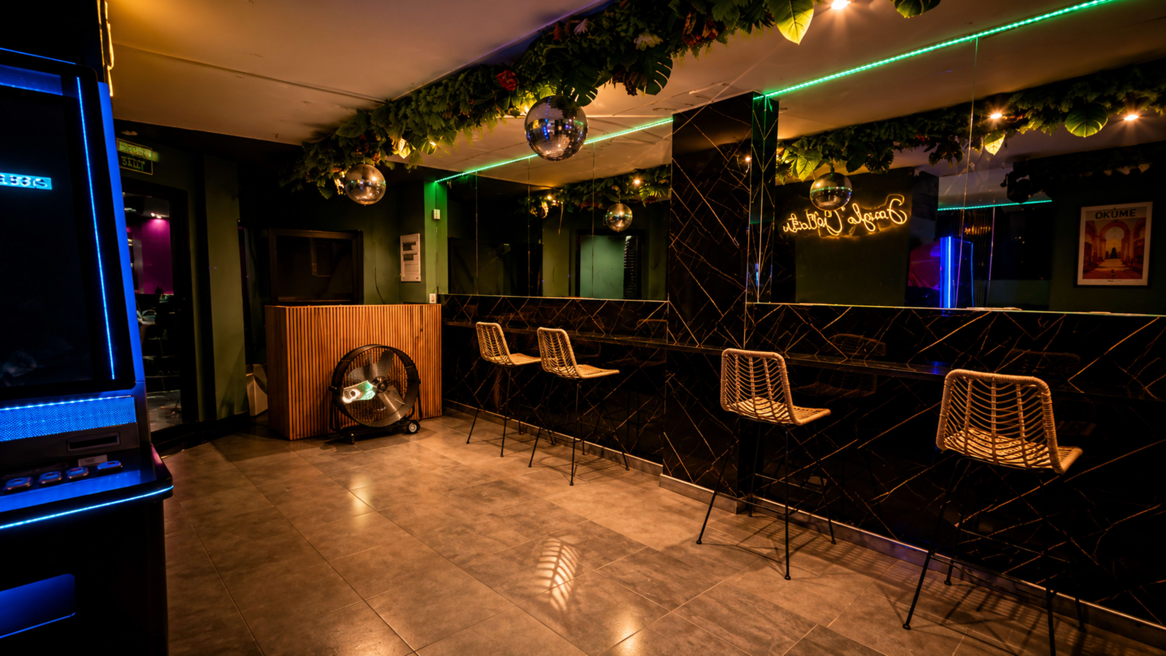 The image shows a modern bar interior with a mirrored wall, glowing LED lighting, and a few empty seats.