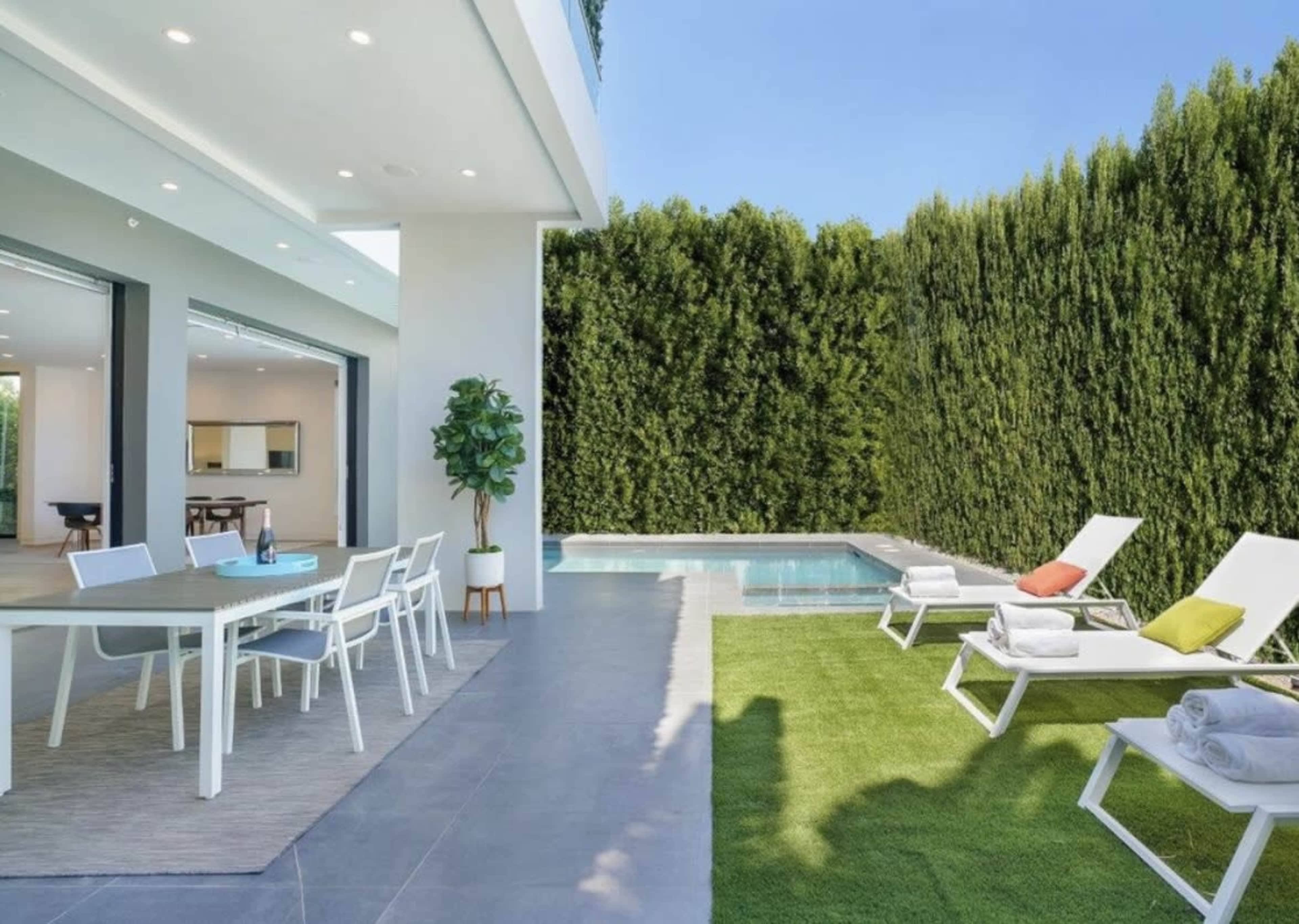 A modern outdoor living space features a swimming pool, lounge chairs, and a dining area adjacent to a neatly manicured lawn.