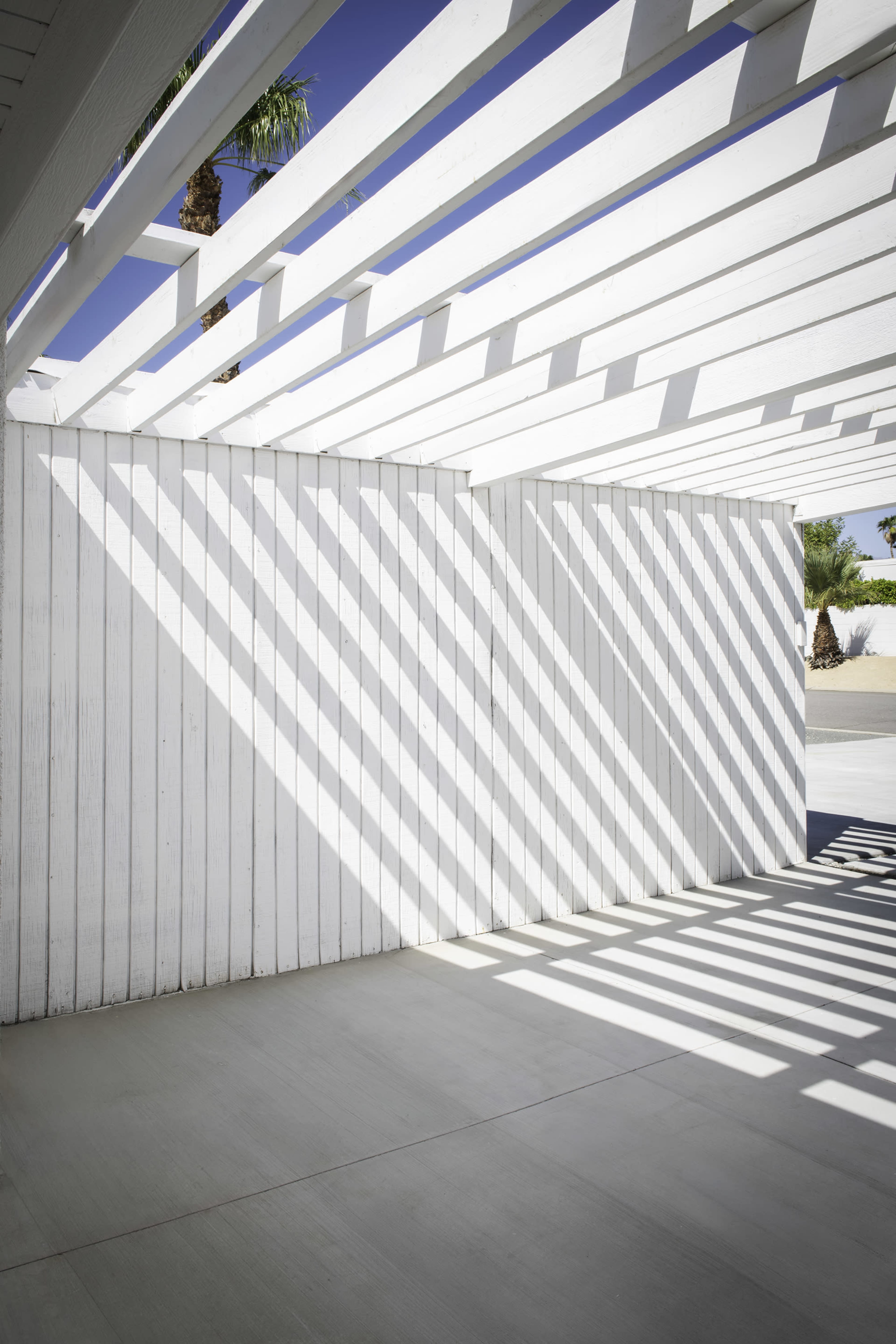 The image shows a white slatted structure casting diagonal shadows on a light-colored floor.