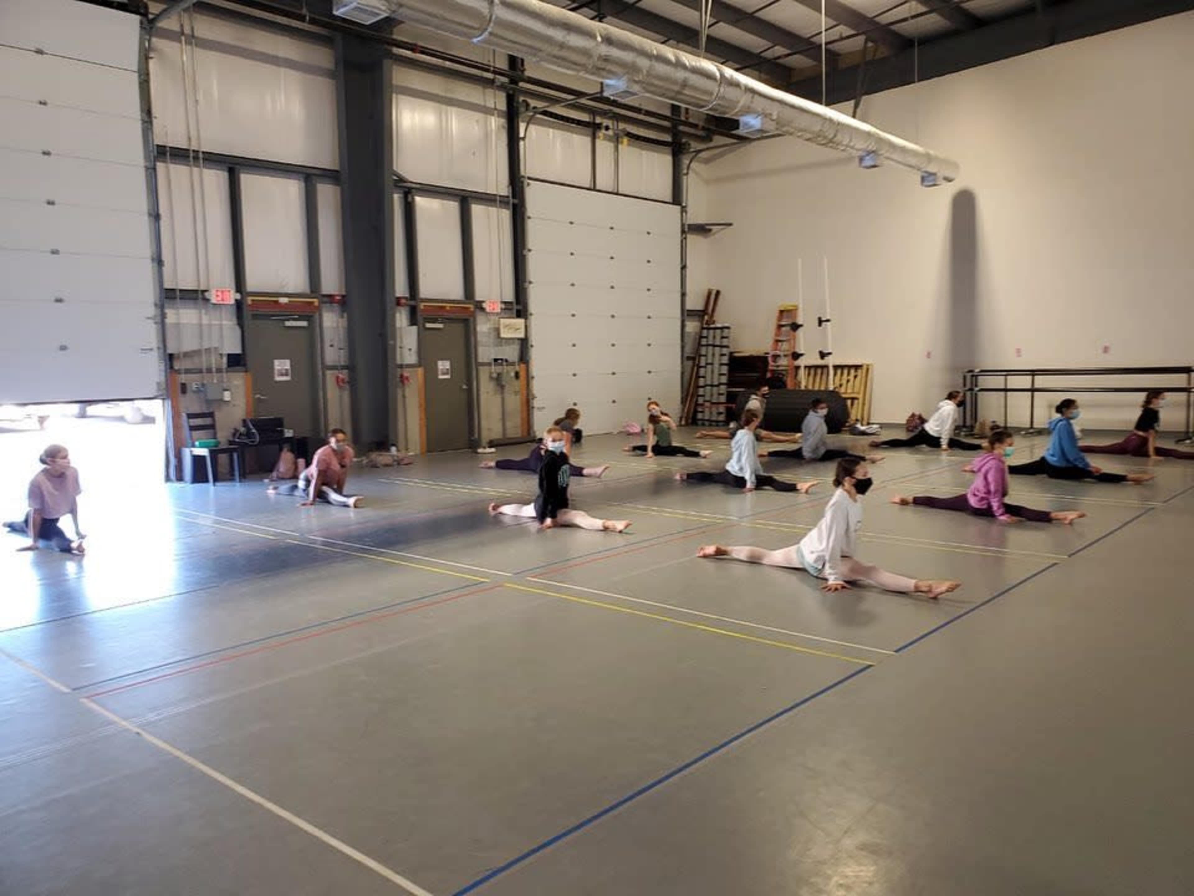 A group of people are practicing splits on a gymnasium floor in a spacious studio.