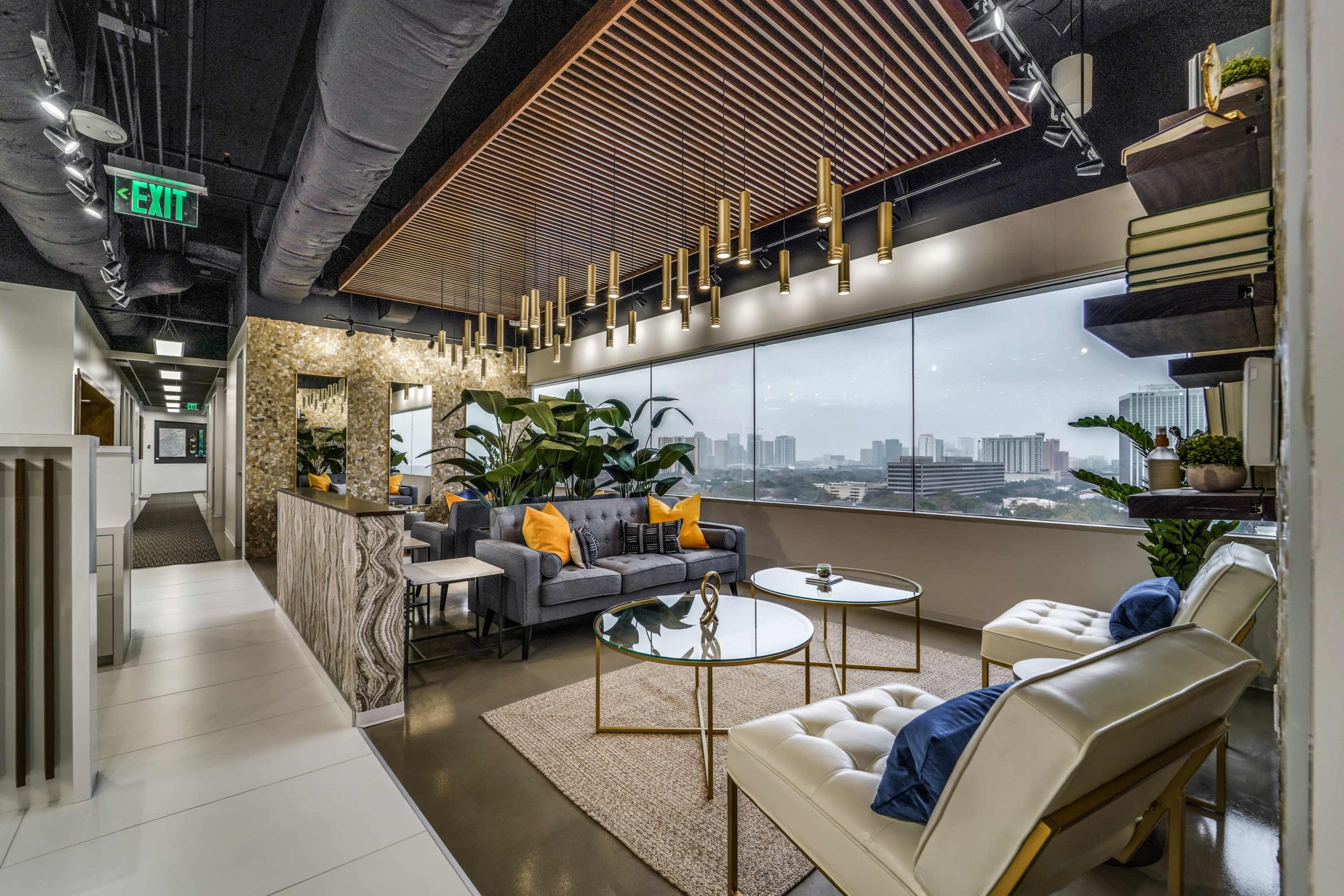 A modern office lounge area with a gray sofa, white chairs, gold accents, and large windows overlooking a city skyline.