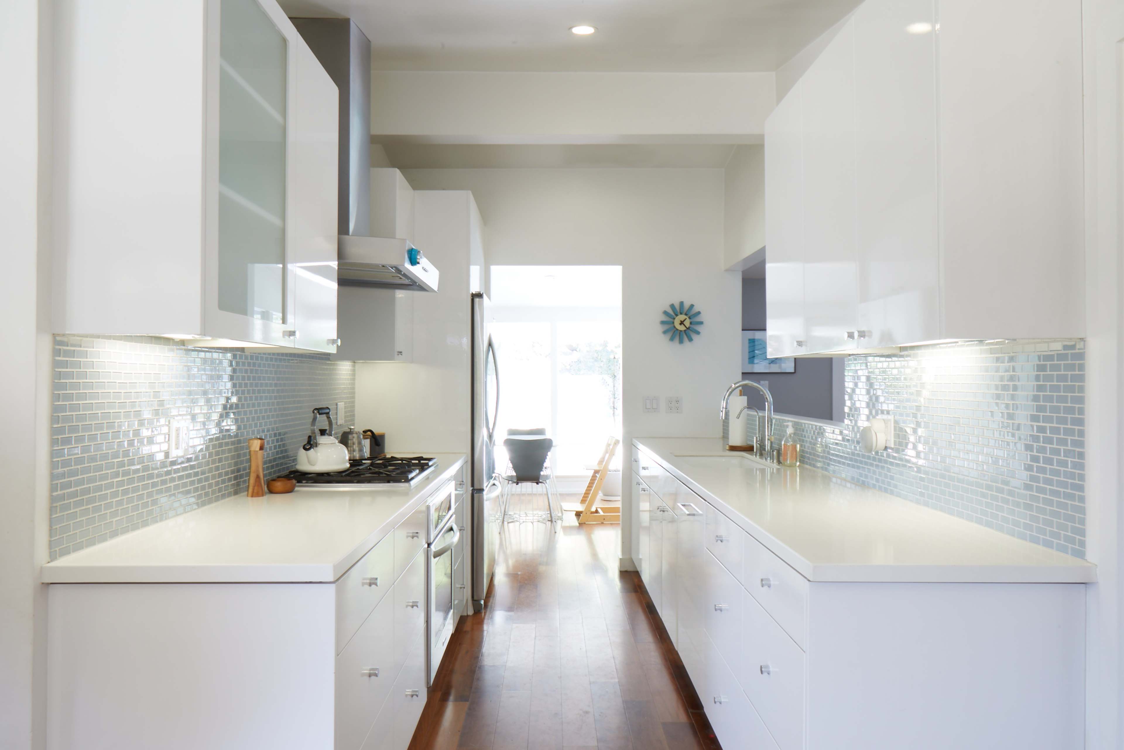 A modern kitchen with white cabinetry, a stainless steel stove, and light-colored countertops, with a tiled backsplash and wooden flooring.