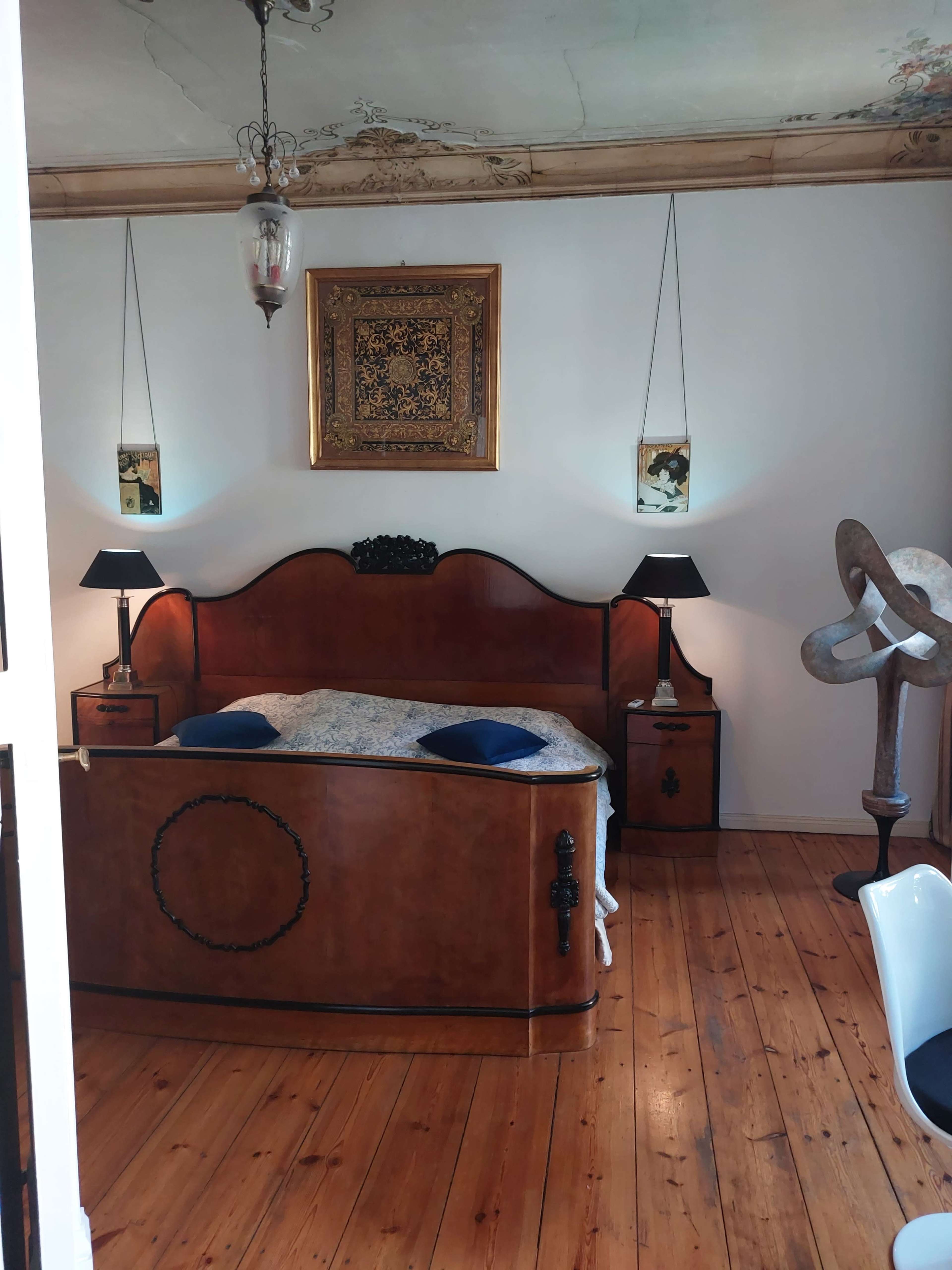 The room features a wooden bed with decorative headboard, bedside lamps on each side, and artwork hanging on the walls.