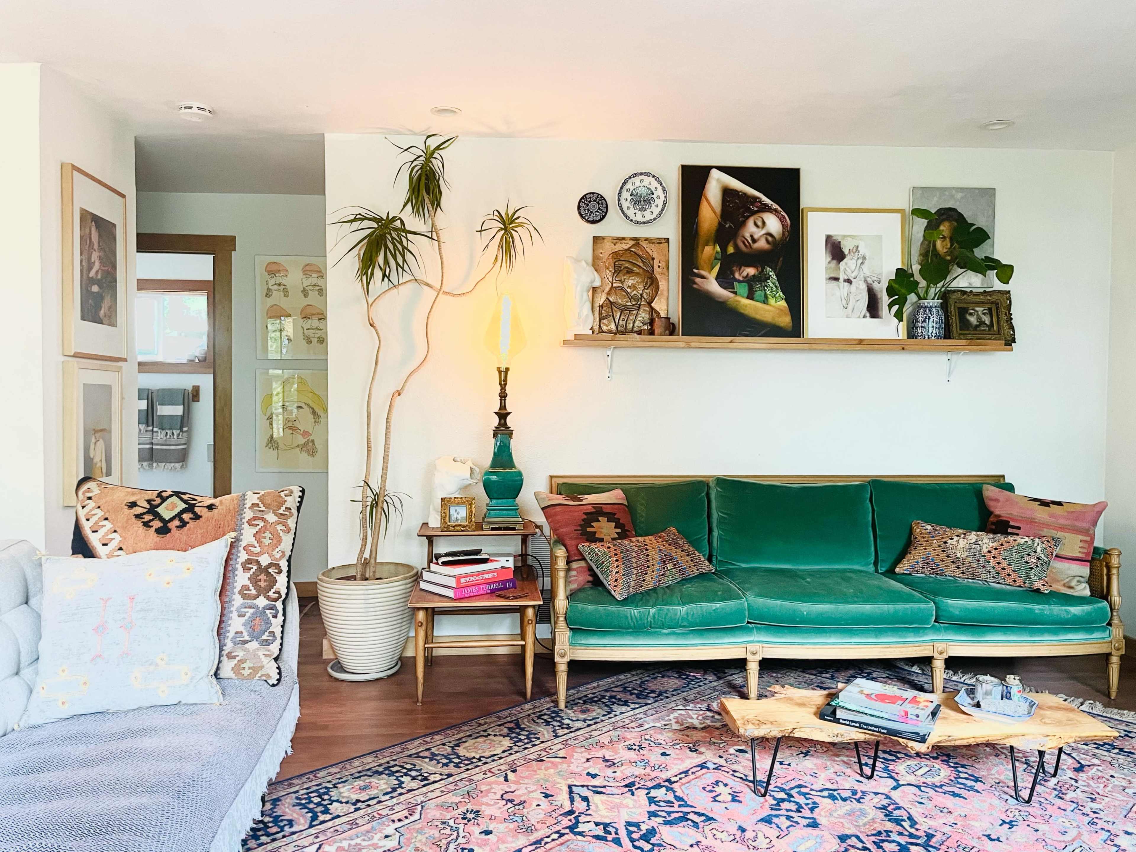 The living room features a green sofa with decorative pillows, a wooden coffee table, and a shelf displaying various artworks and plants.