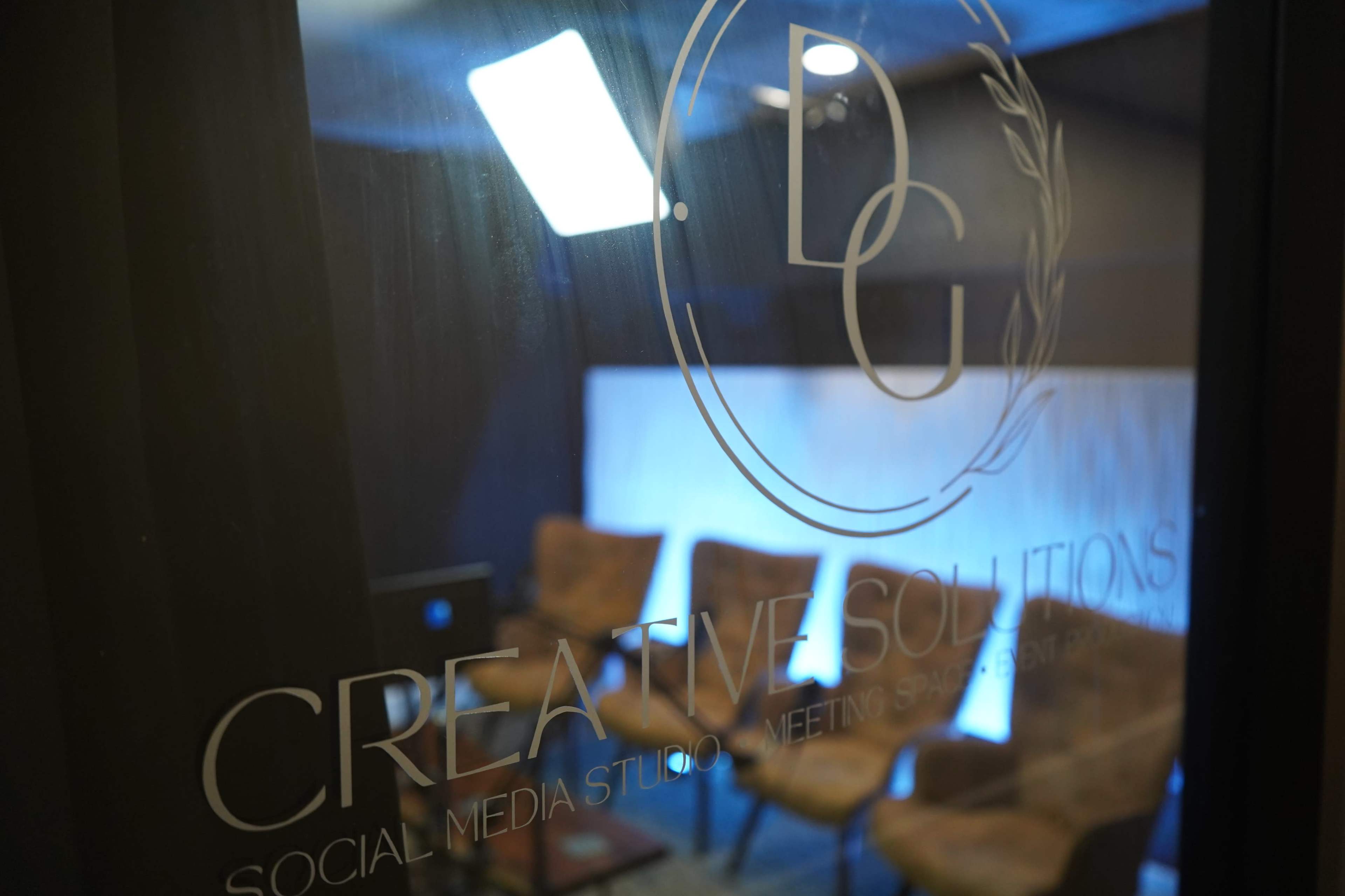 The image shows a studio space with a sign for "Creative Solutions" and several empty chairs arranged in front of a lit backdrop.
