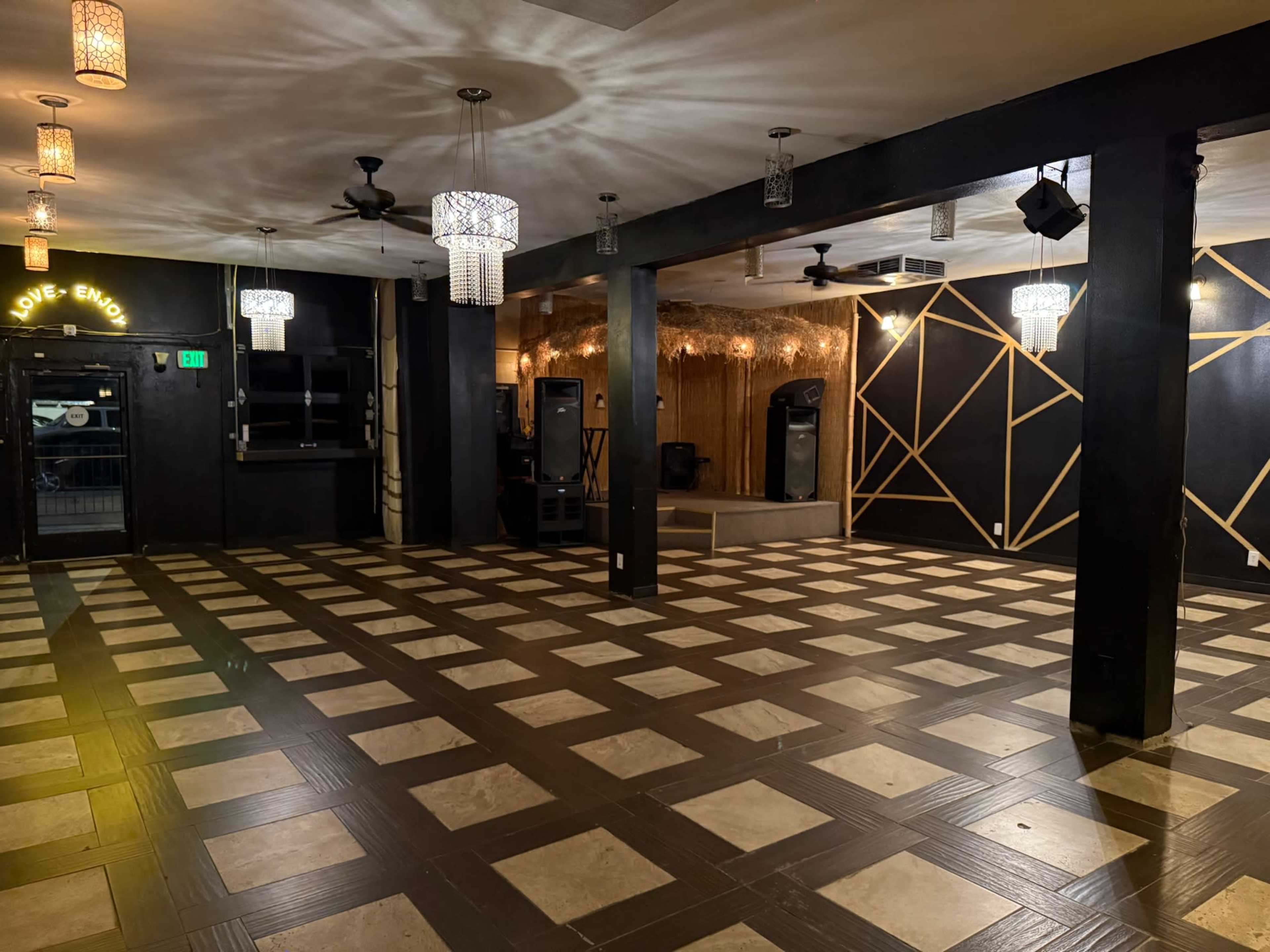 The image shows an empty event space with a patterned tile floor, a stage area, and decorative lighting fixtures.