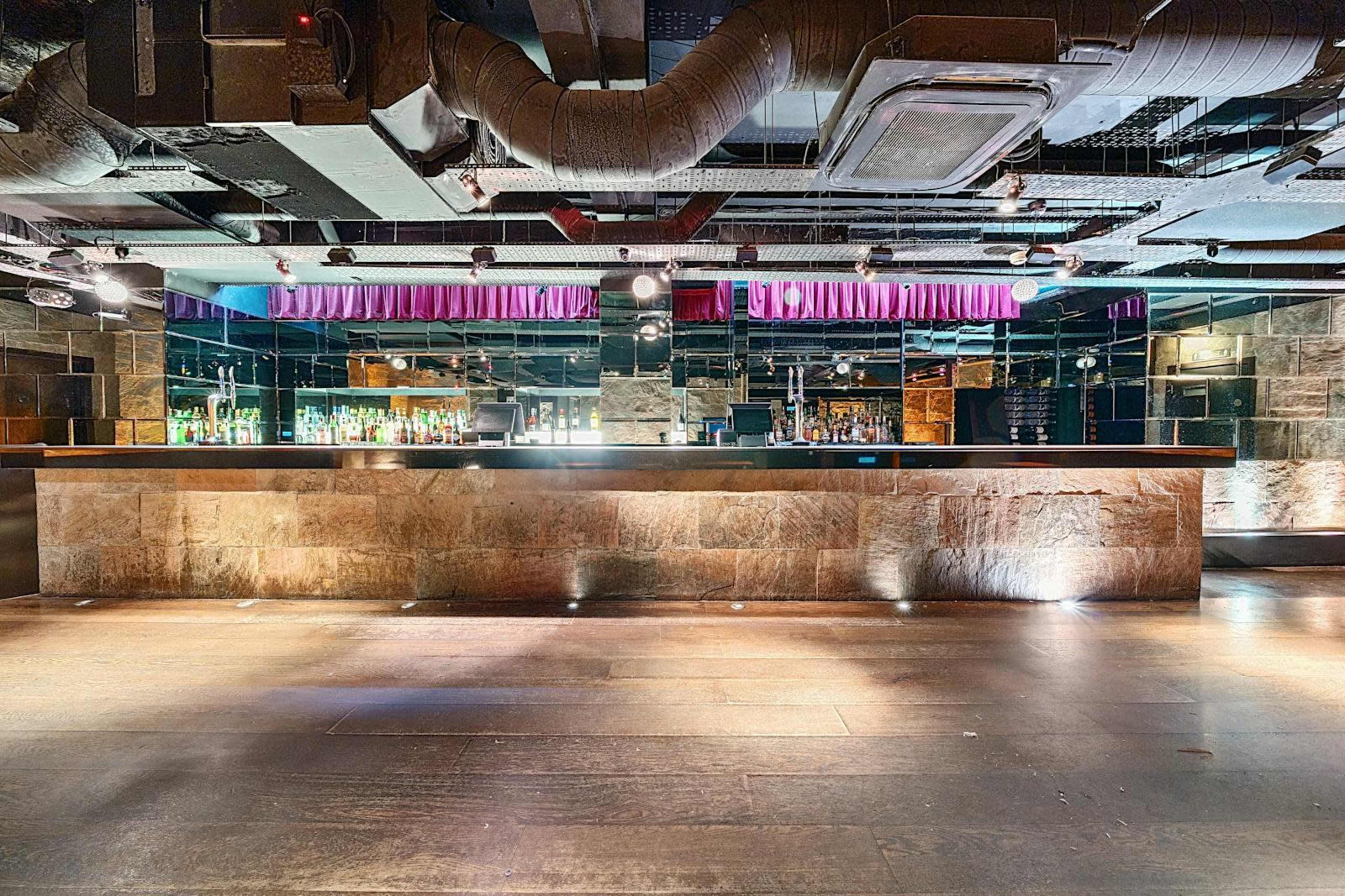 The image shows a spacious, modern bar area with a long stone counter and a mirrored background, illuminated by soft lighting.