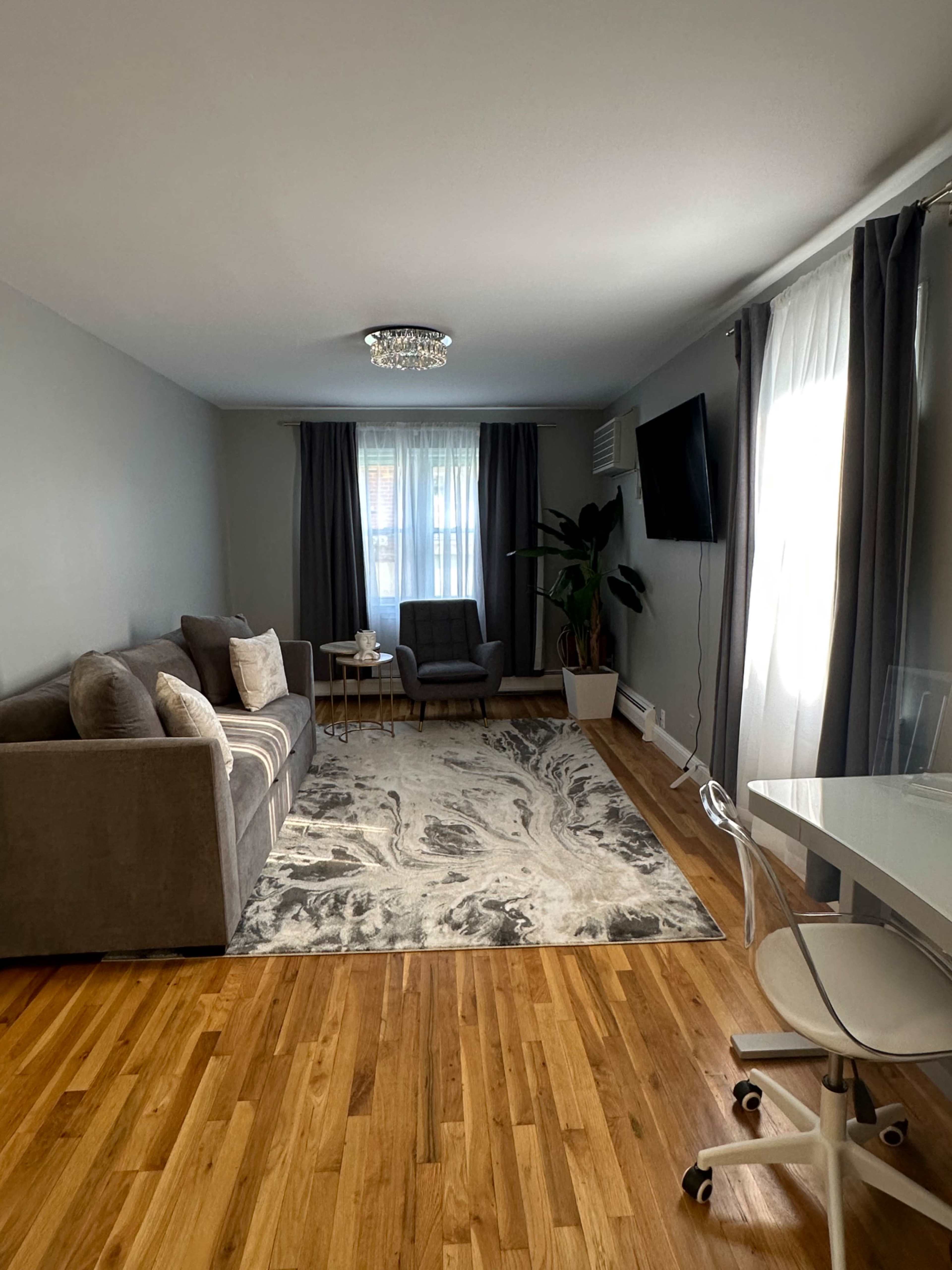 A modern living room with a gray sofa, a coffee table, two armchairs, a large area rug, and a flat-screen TV on the wall.