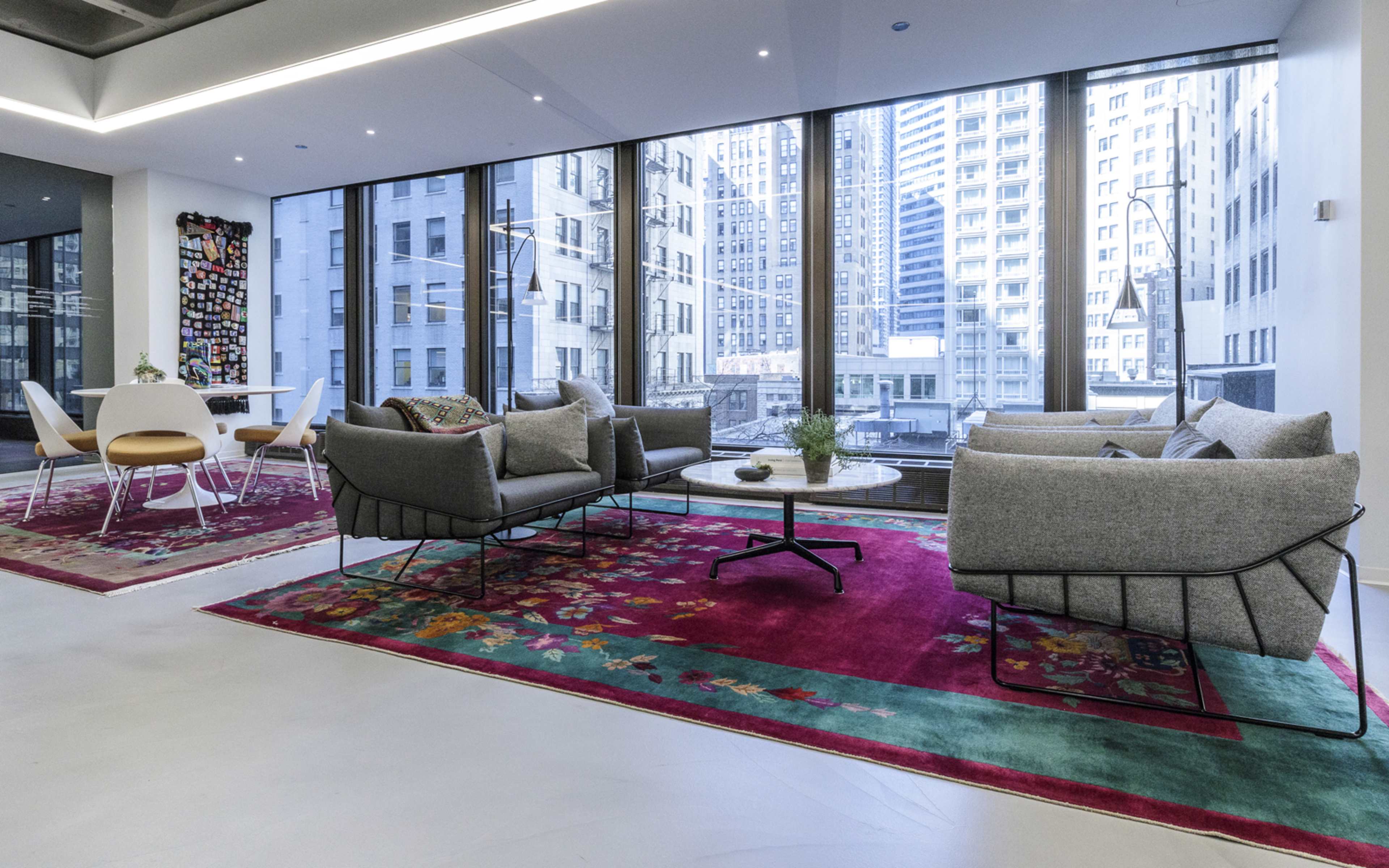 A modern office interior with two gray sofas and a circular table, set against large windows that reveal a cityscape.