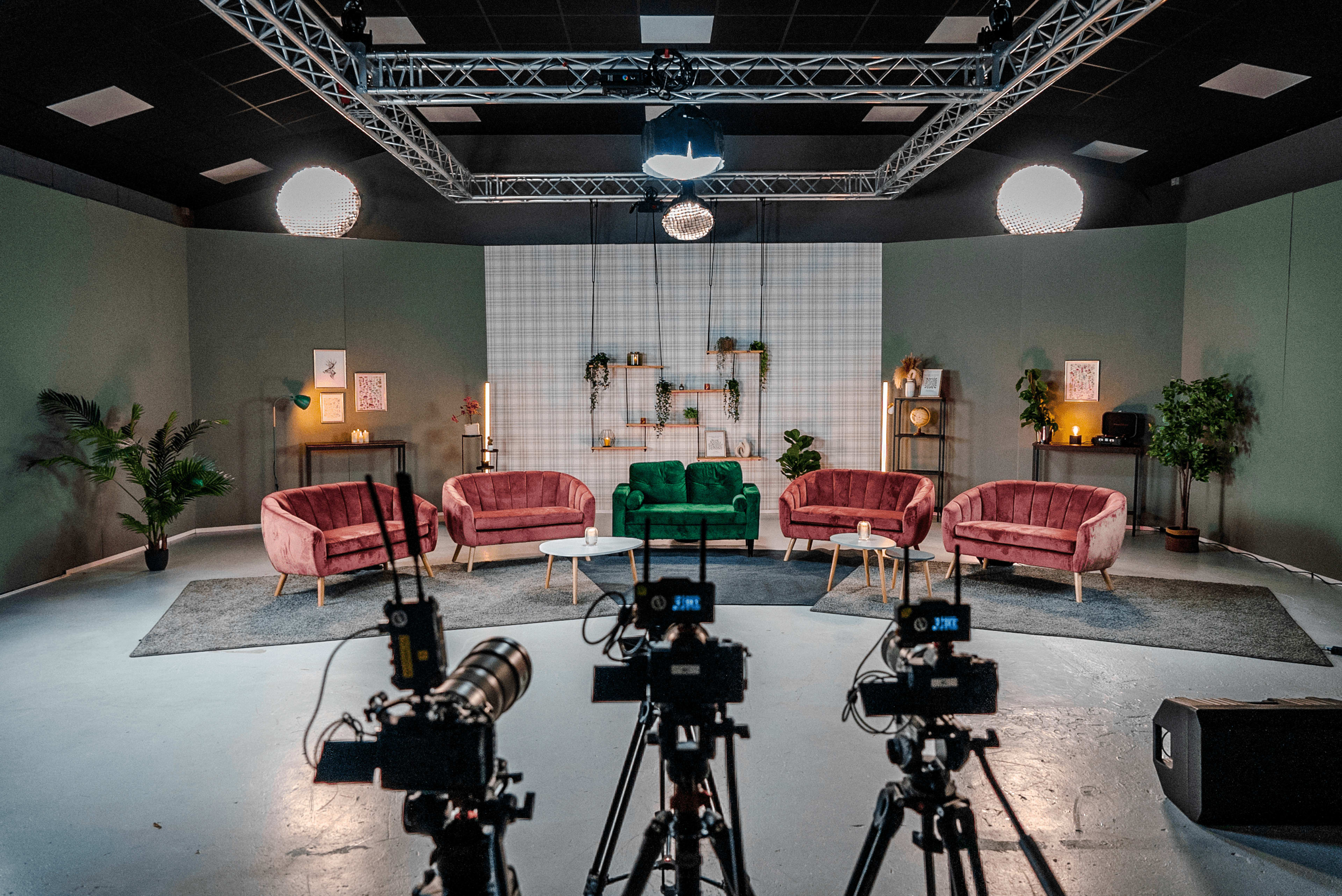 A television studio set features multiple sofas arranged in a semi-circle with cameras positioned in front.