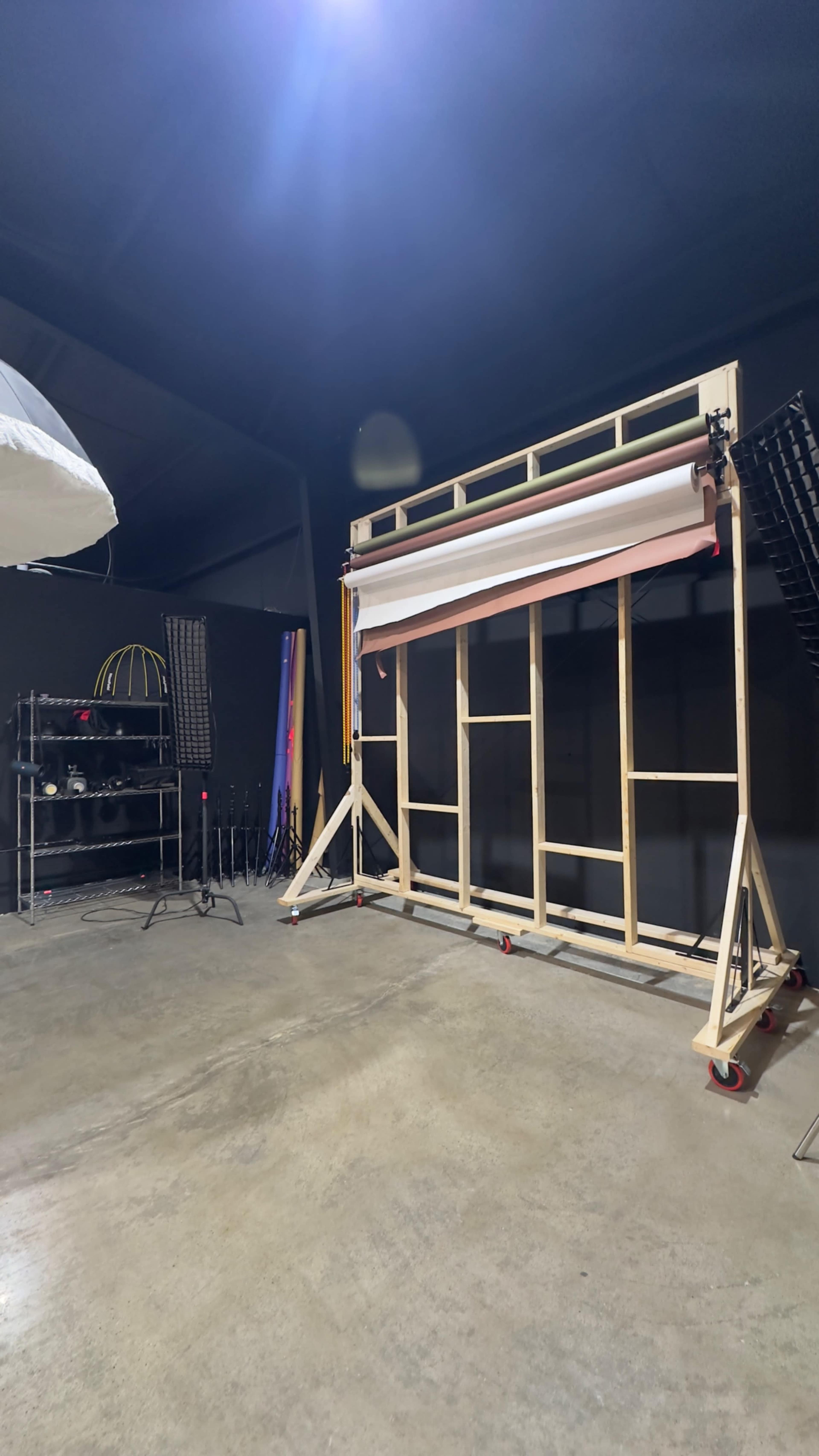 The image shows a photography studio setup with a large backdrop support frame on wheels and various film equipment against a bare concrete floor.