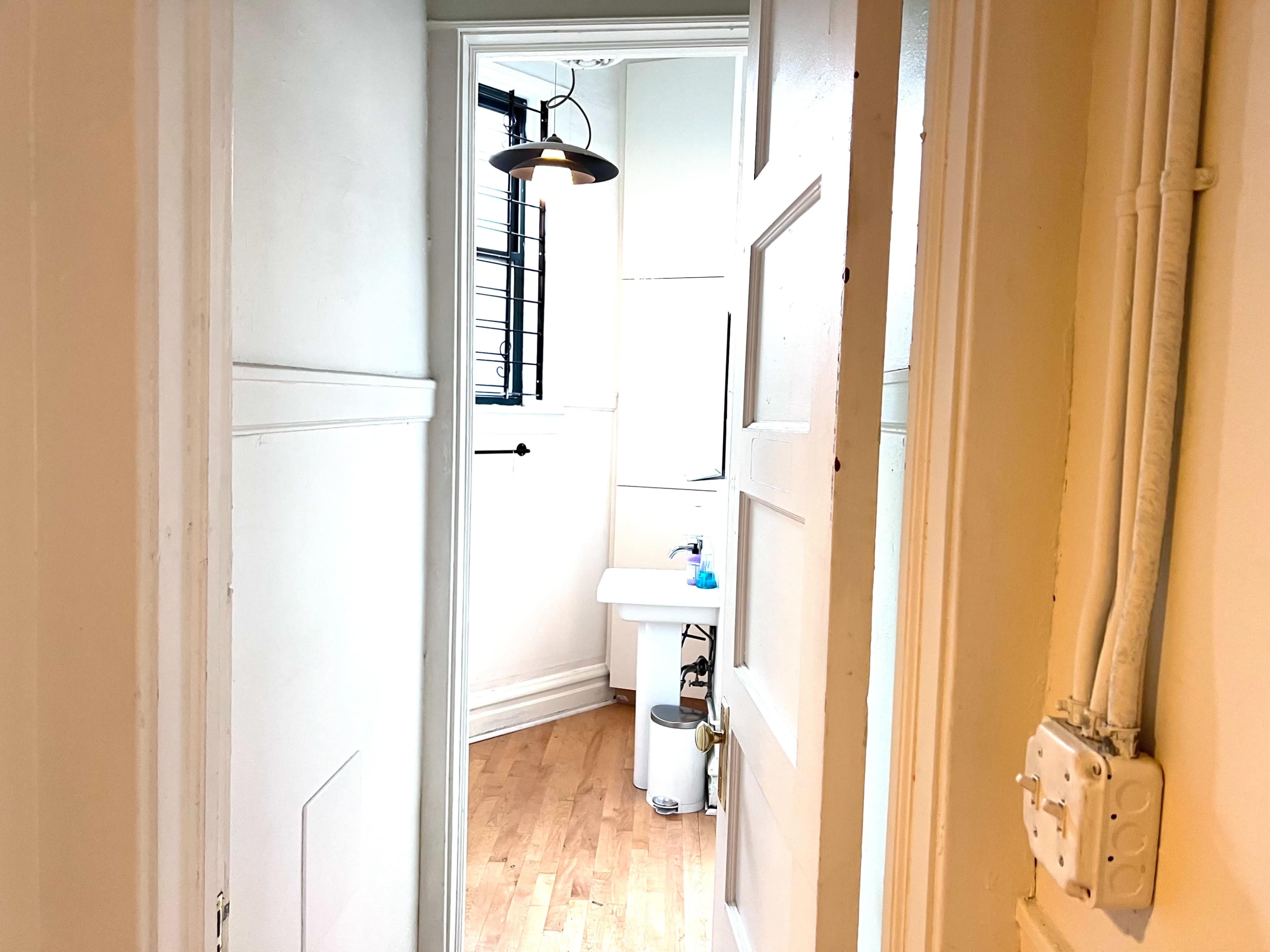 The image shows a narrow hallway leading to a small room with a white table and a window.