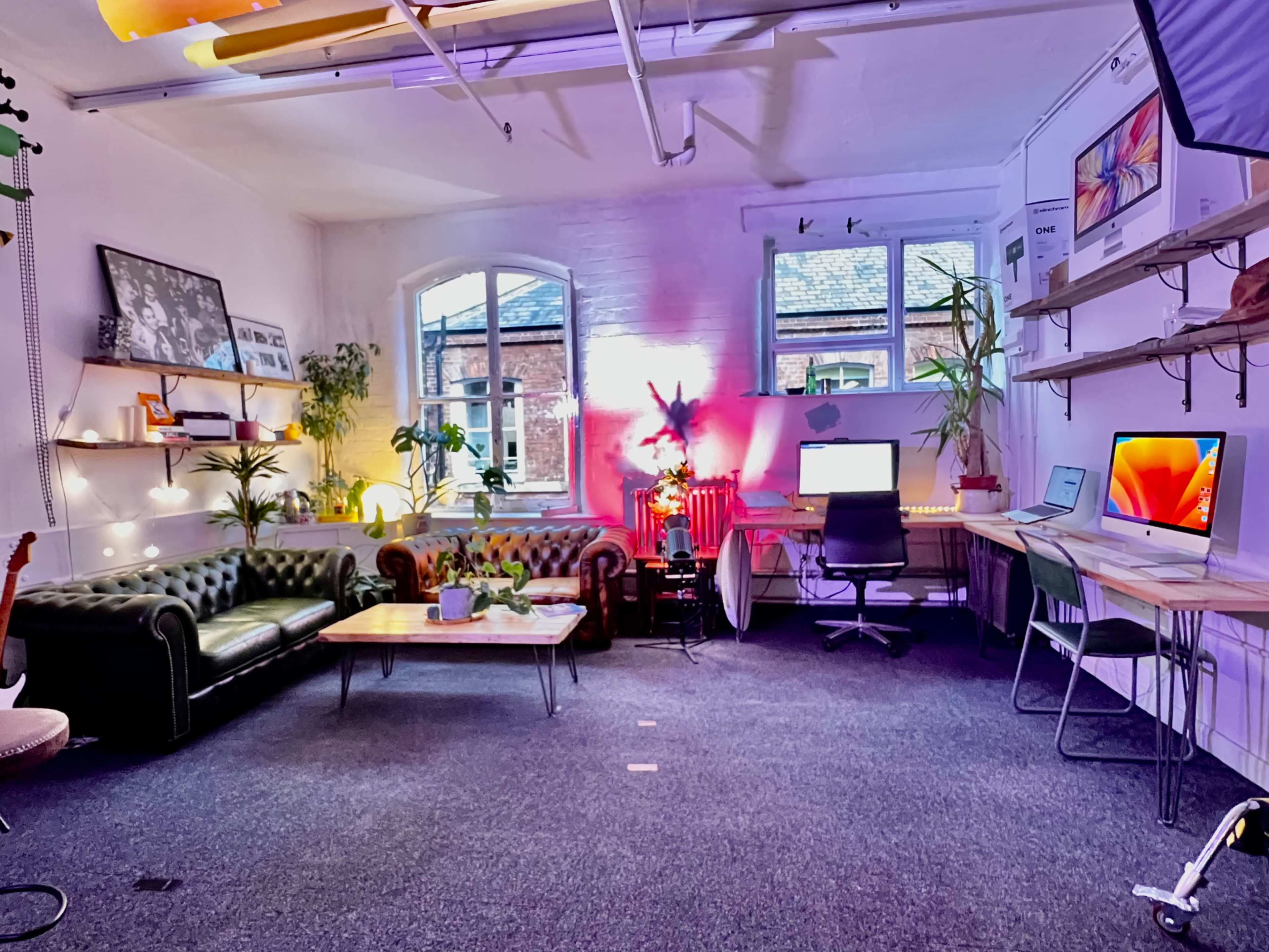 A modern, well-lit office space featuring a green leather sofa, plants, and multiple workstations with computers.
