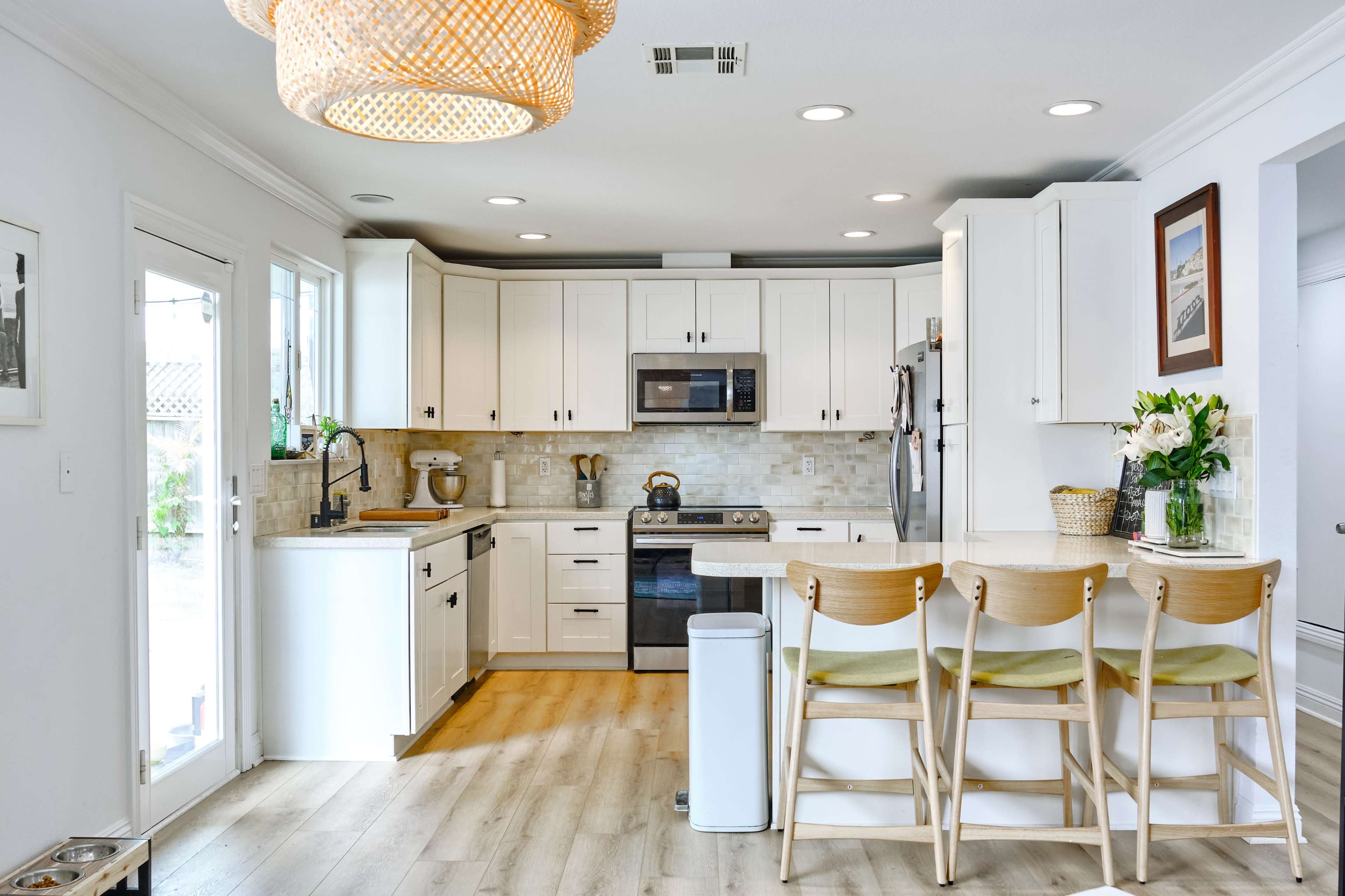 A modern kitchen with white cabinetry, stainless steel appliances, and a breakfast bar with three wooden stools.