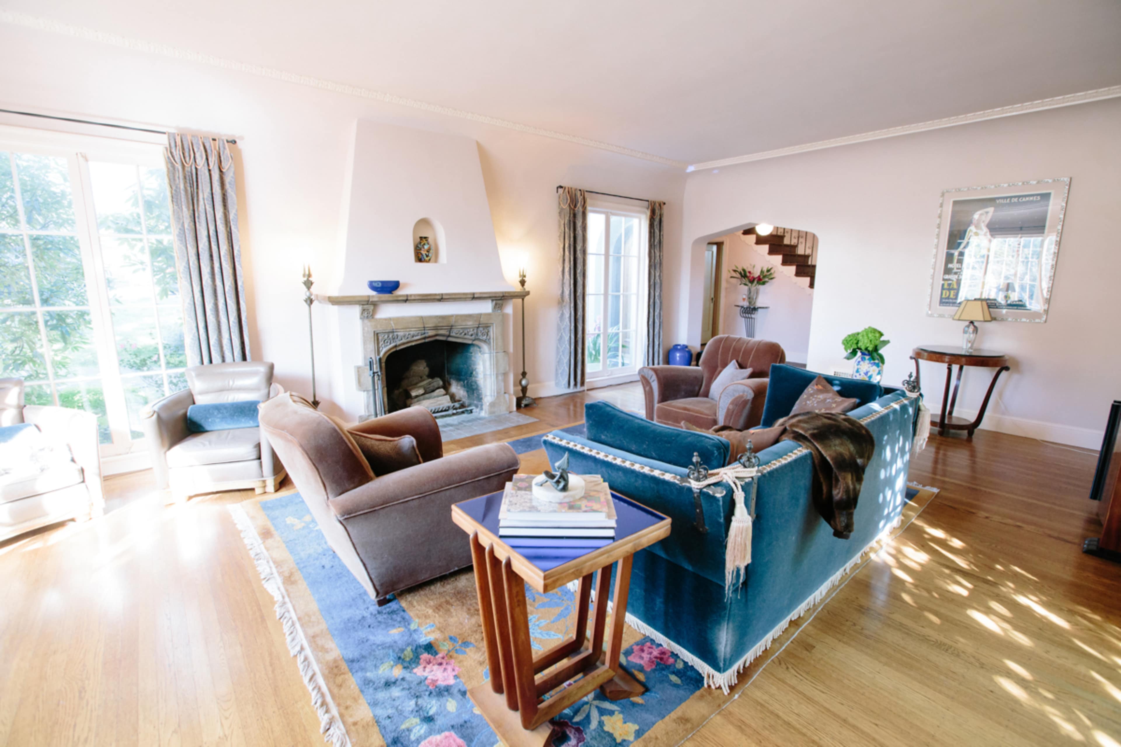 The living room features a blue velvet sofa, brown armchairs, and a fireplace, with large windows allowing natural light to fill the space.