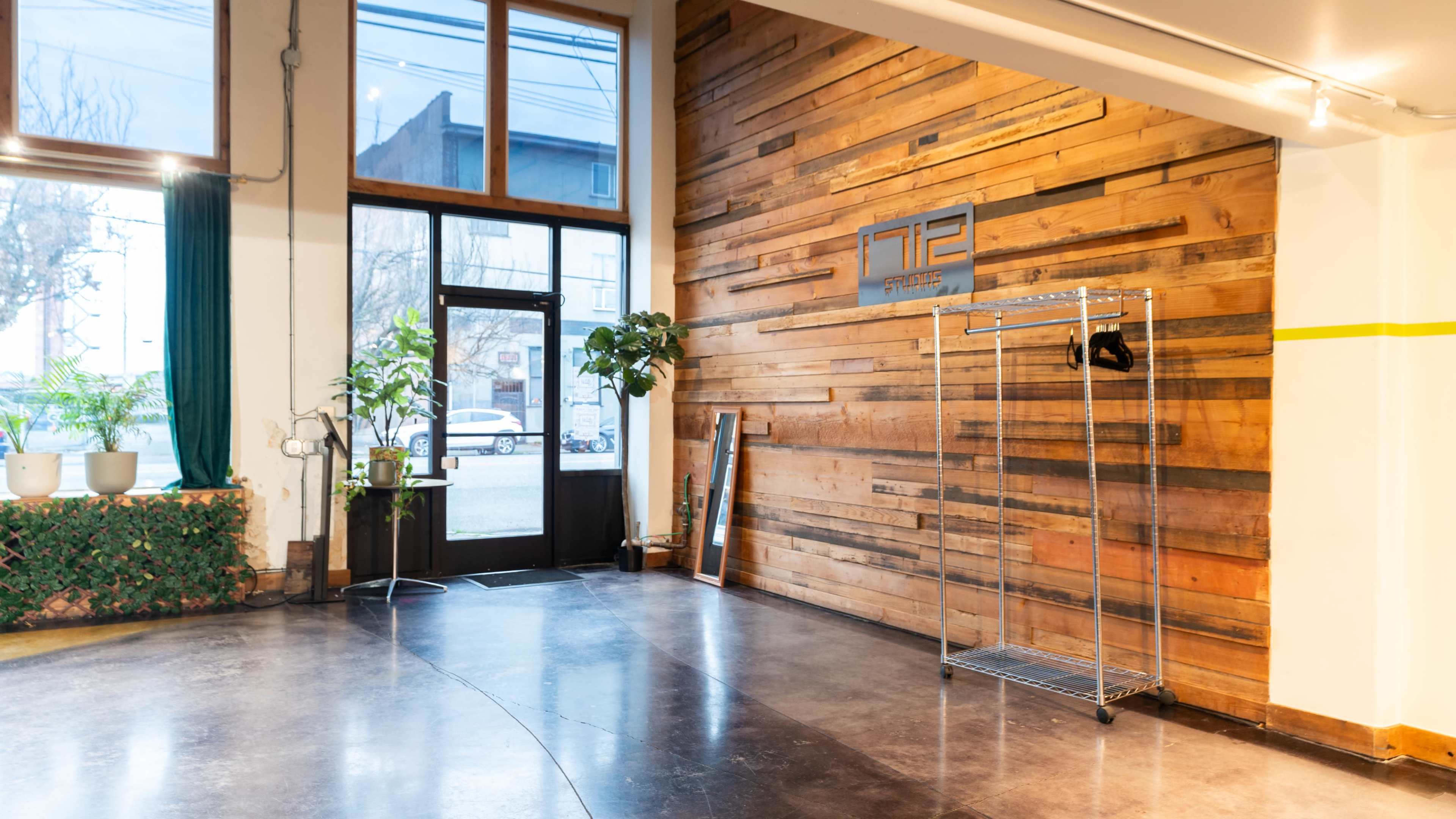 The image shows a modern interior space with a wooden accent wall, a large window, and a metal clothing rack in the corner.