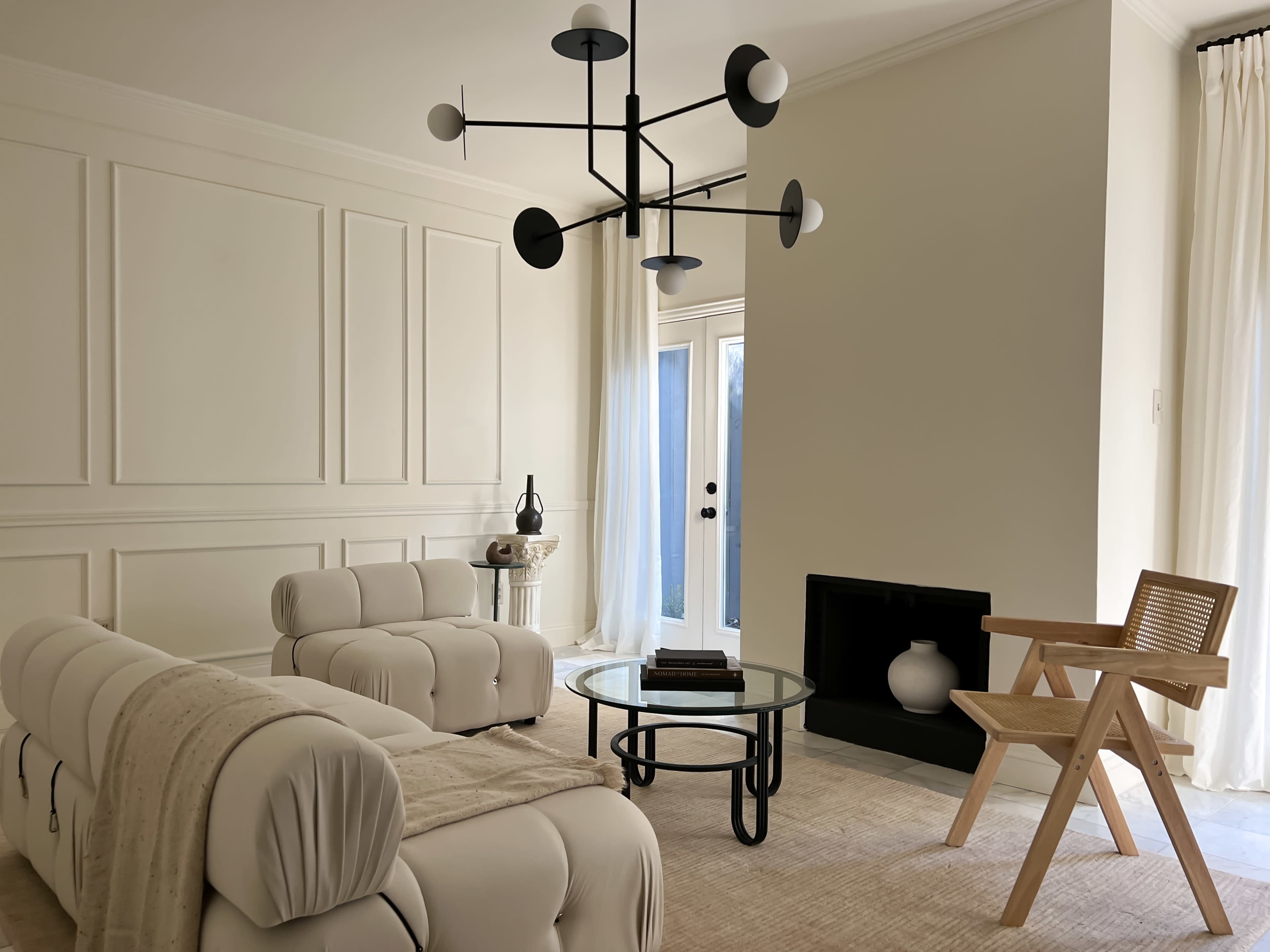 The living room features a modern design with a white sectional sofa, a round glass coffee table, a minimalist chandelier, and a wooden chair near a fireplace.