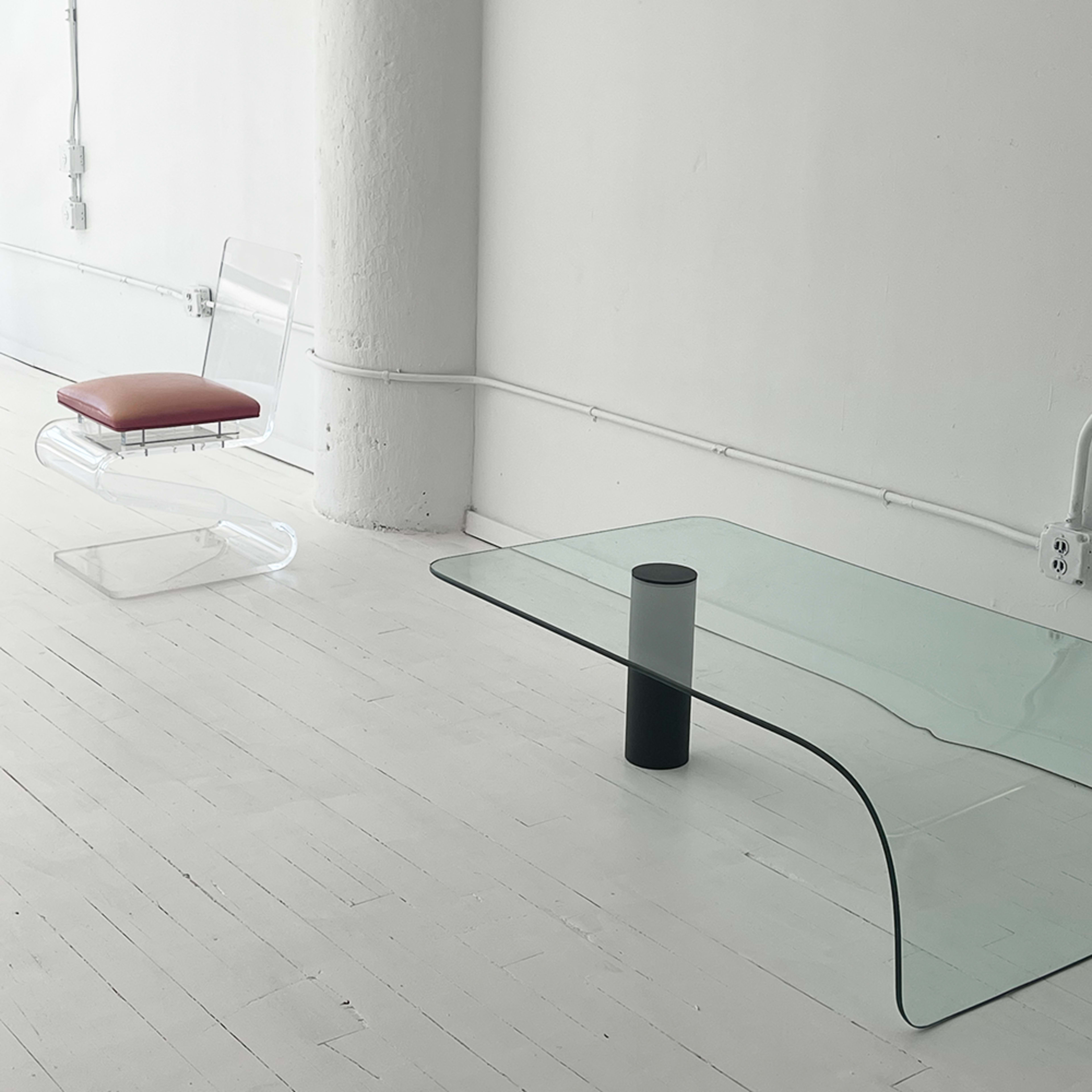 A minimalist interior with a transparent chair and a curved glass coffee table on a white wooden floor.
