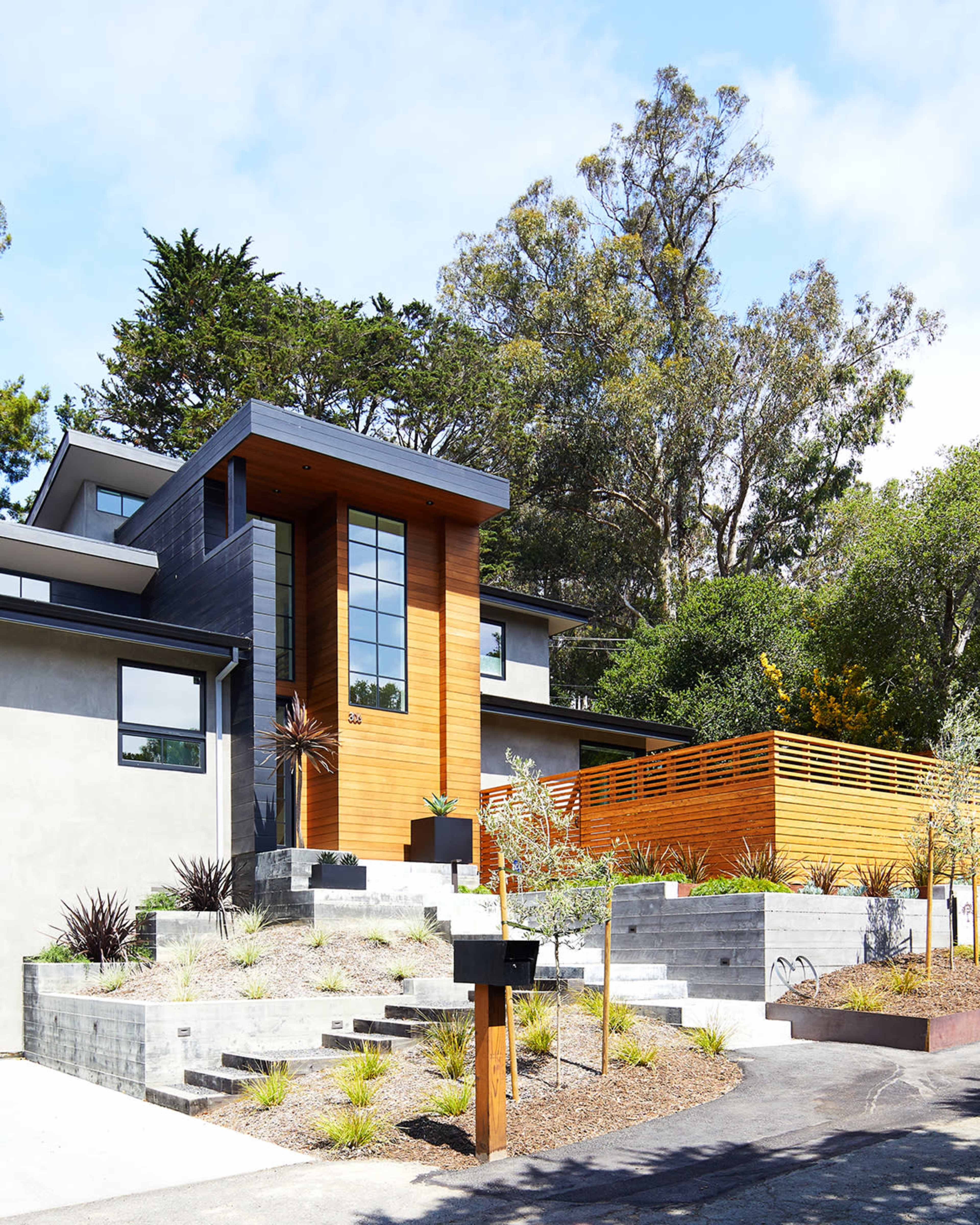 A contemporary house features a combination of wood and concrete elements, with landscaped steps leading to the entrance.